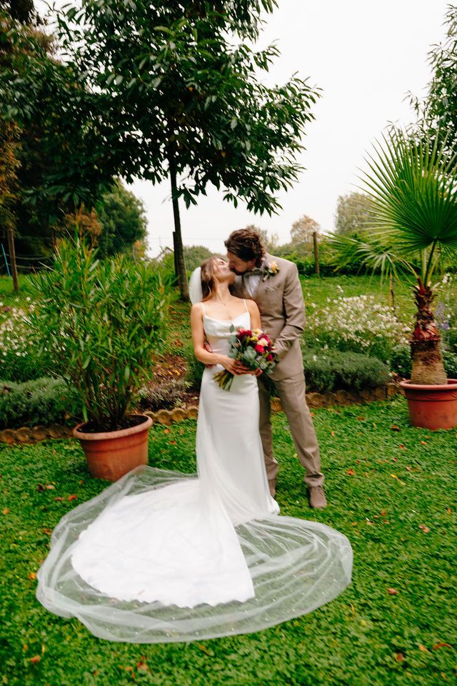 A couple shares a romantic moment in a lush garden setting with tropical plants and greenery surrounding them.