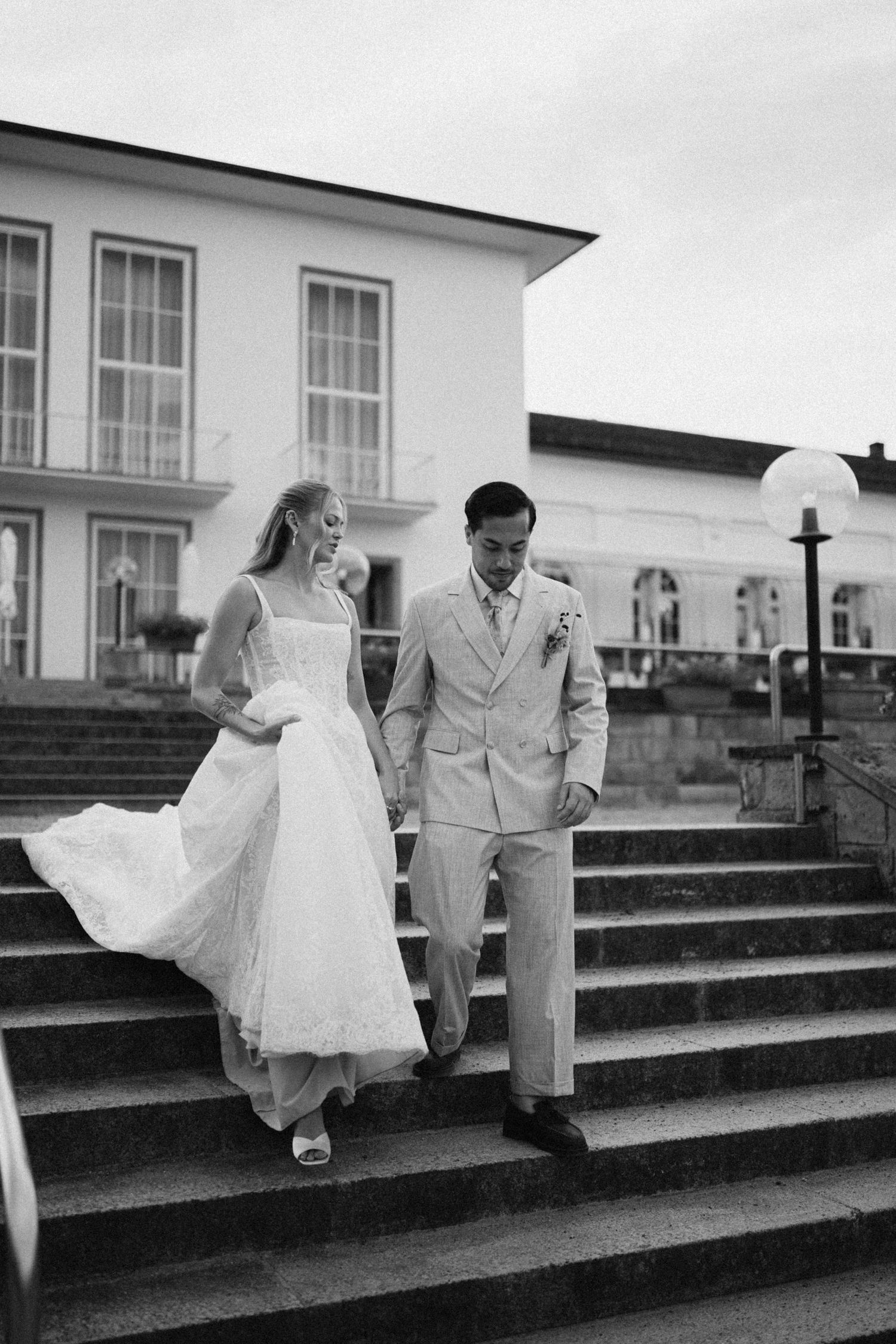 Bride and groom walking down steps hand in hand at classic wedding venue in black and white photo.