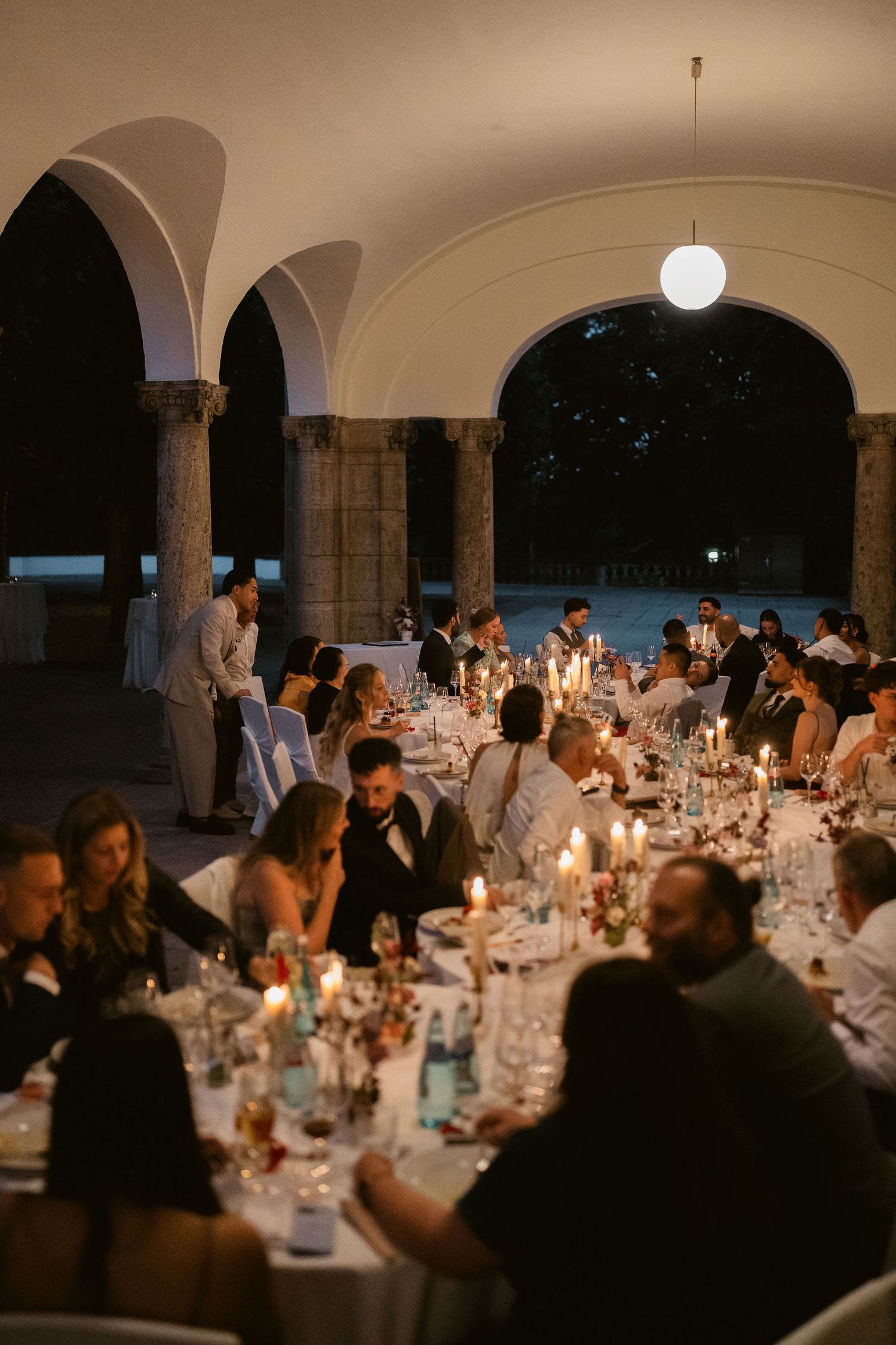 Elegant candlelit wedding reception dinner under arched stone venue with guests seated at long tables.