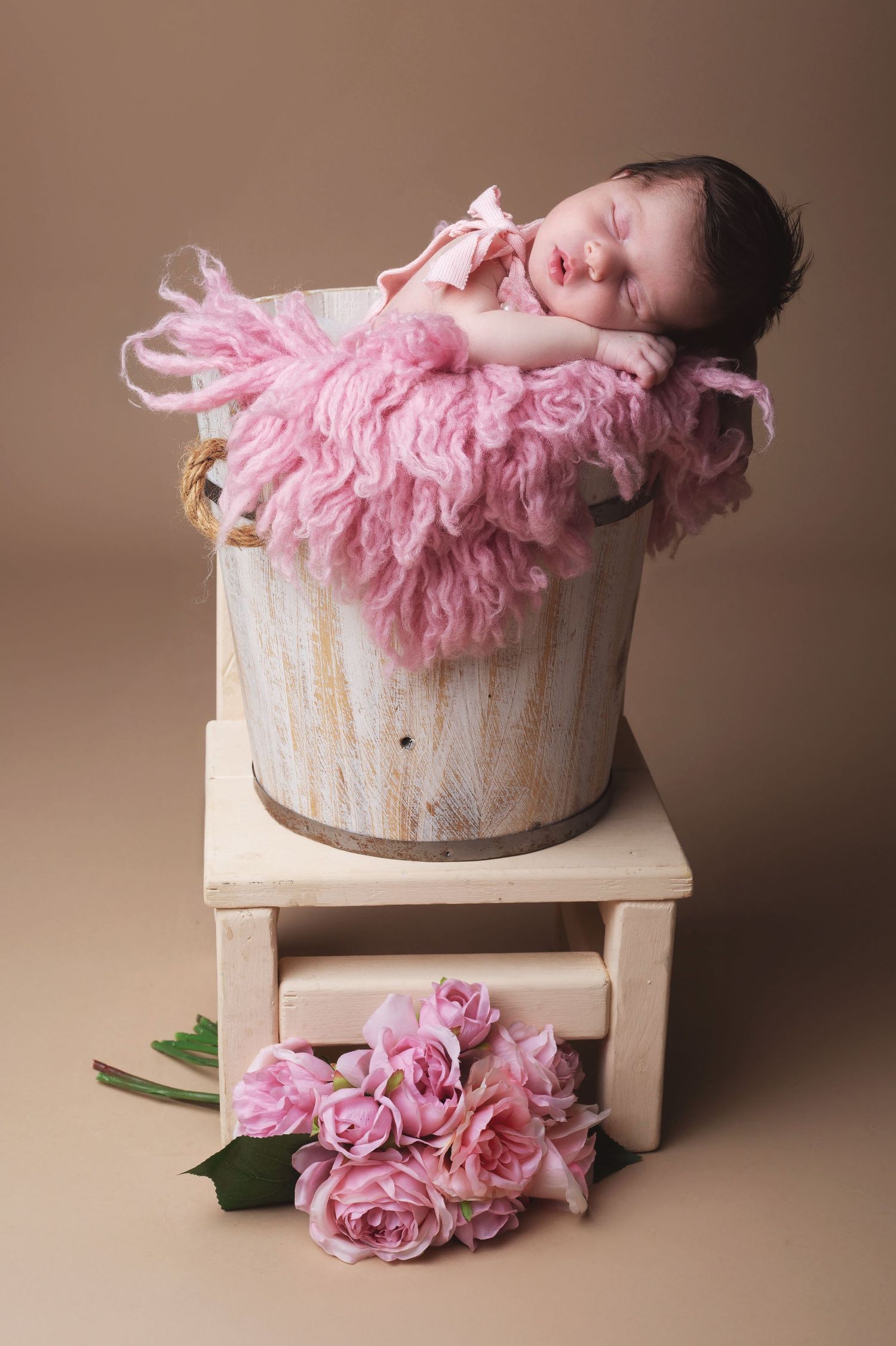 Newborn photography series with pink floral decorations and a rustic wooden prop on neutral brown background.