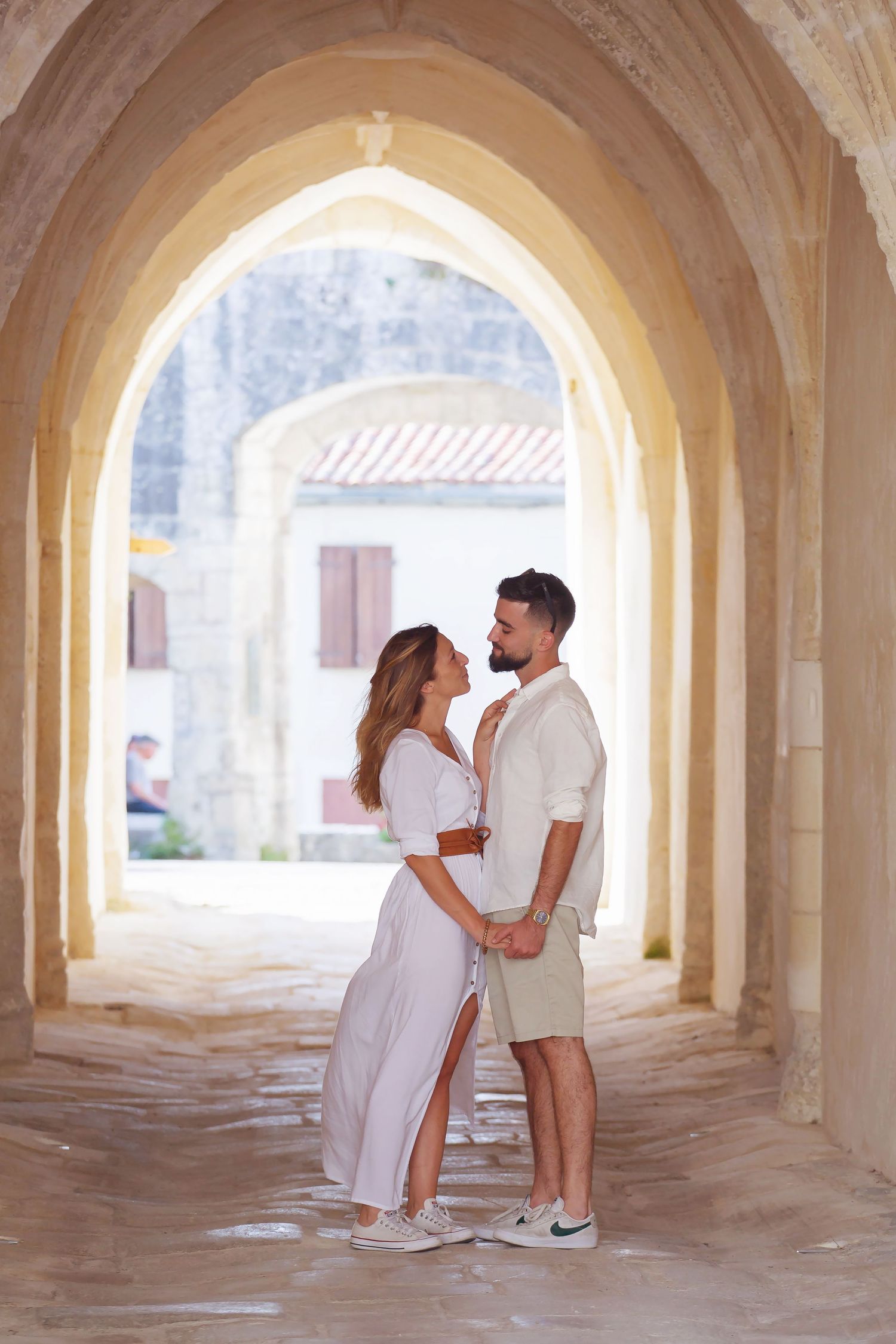 A romantic couple shares tender moments under a series of arched stone passageways in soft natural light.