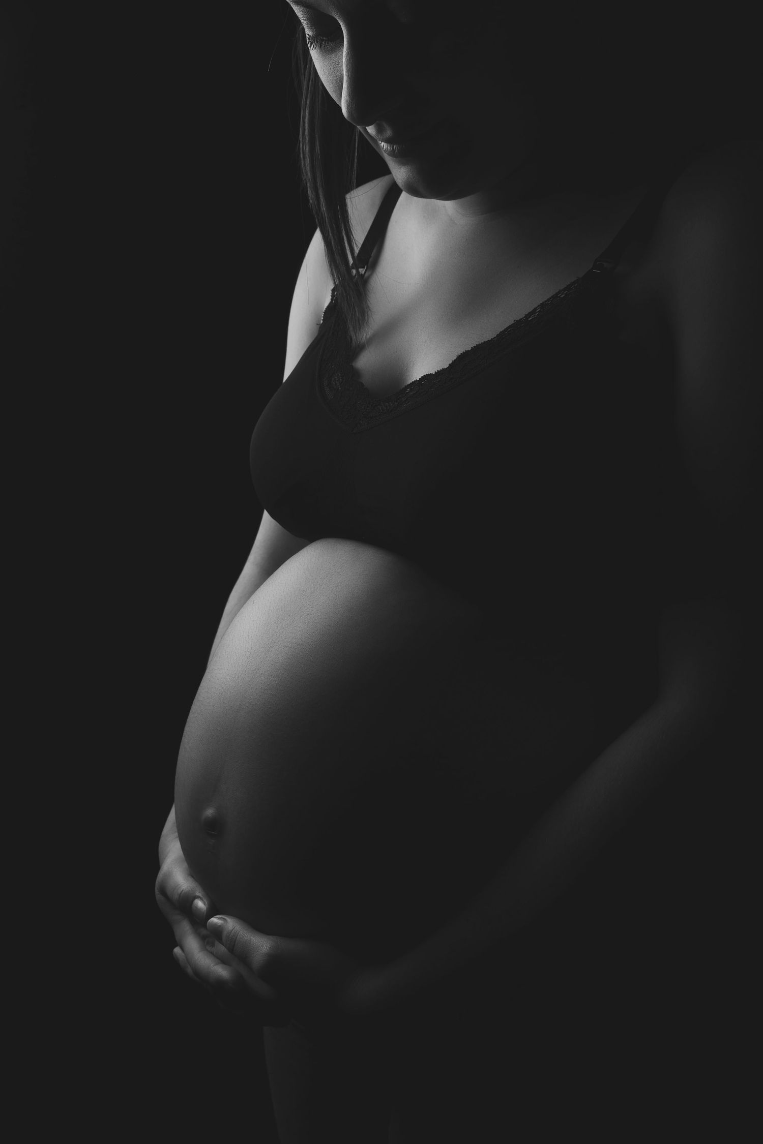 Artistic black and white maternity photo showing silhouette of pregnant belly against dark background.