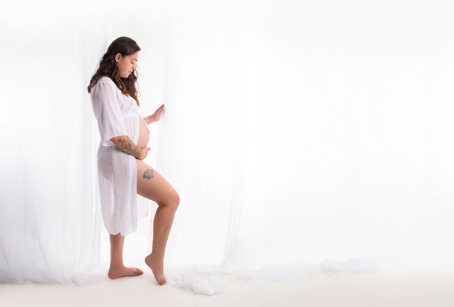 Woman in white dress dancing elegantly in a bright studio setting with ethereal lighting and flowing fabric.