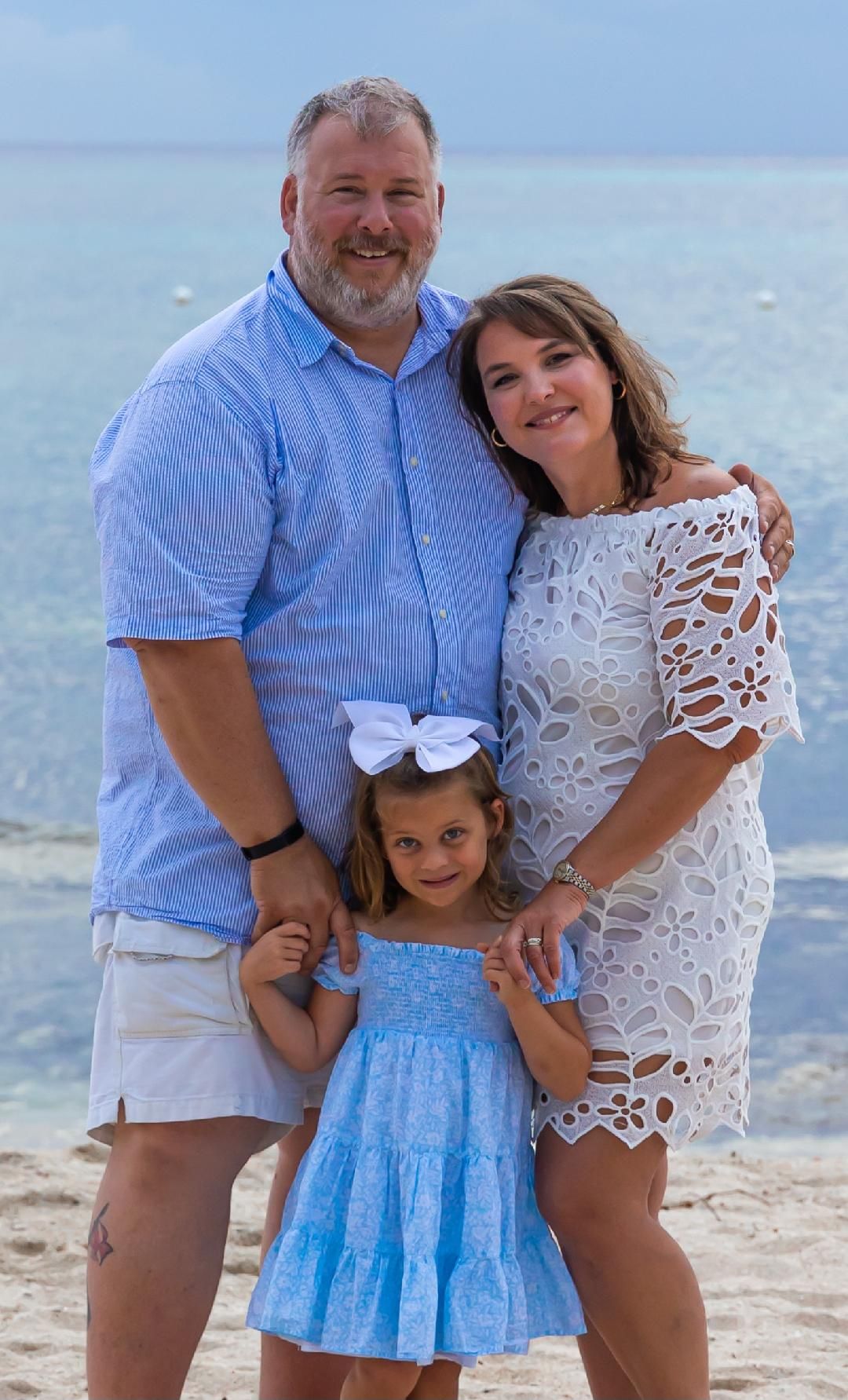 Family poses together on beach with ocean in background.