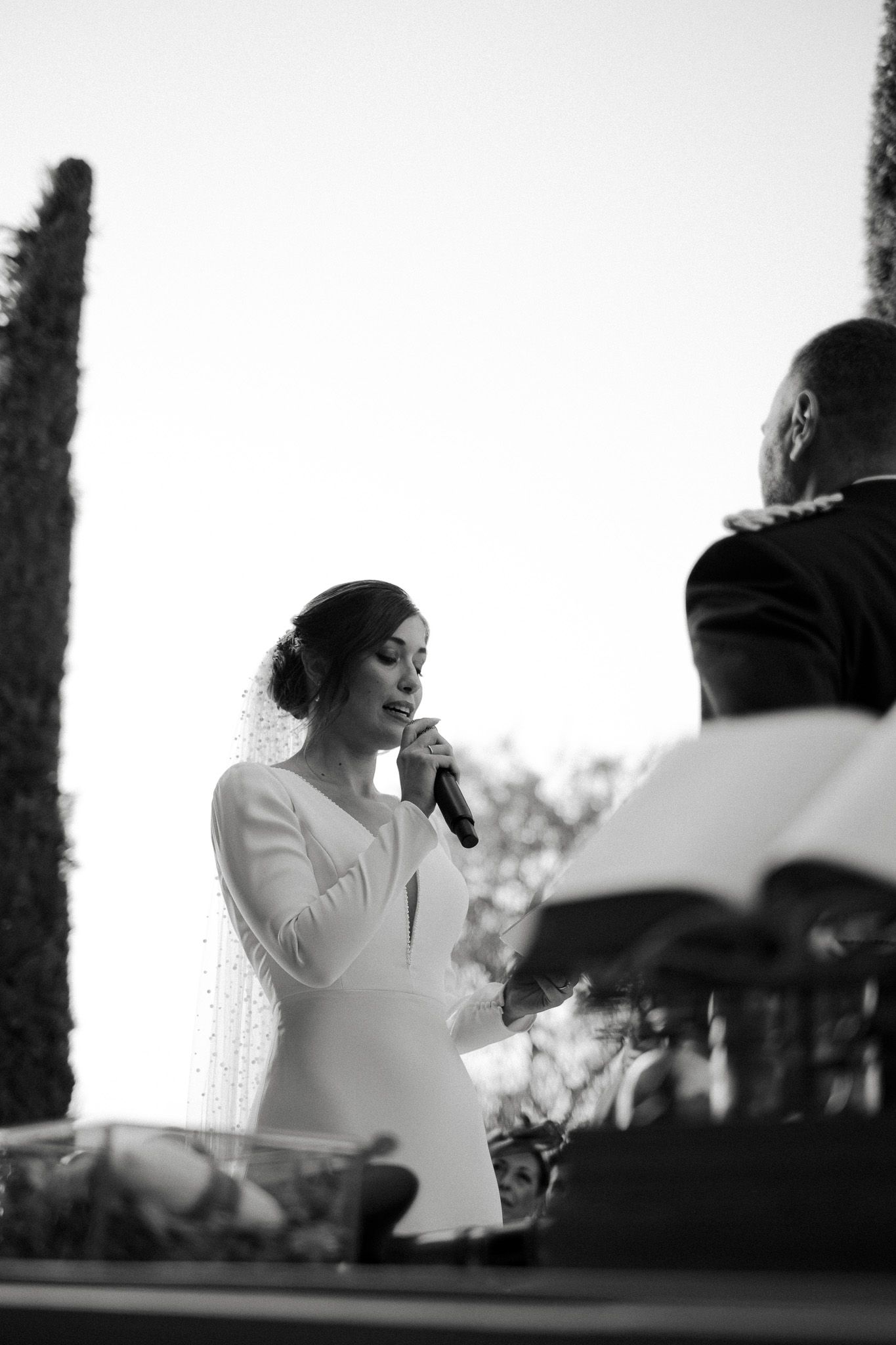 Black and white photo of bride giving a speech during outdoor wedding reception.