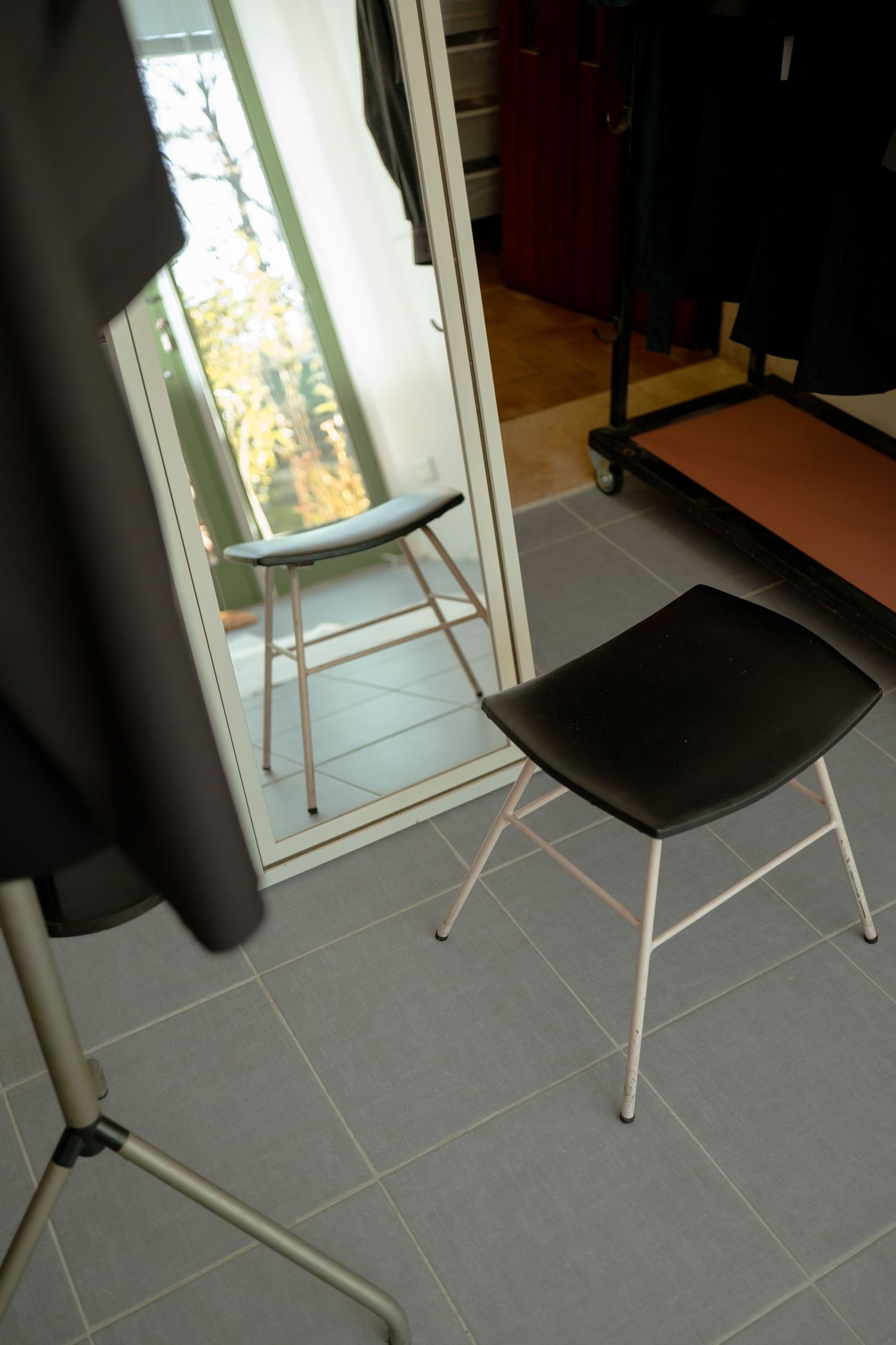 Gray tiled floor with a black chair against a white wall and window showing natural daylight.
