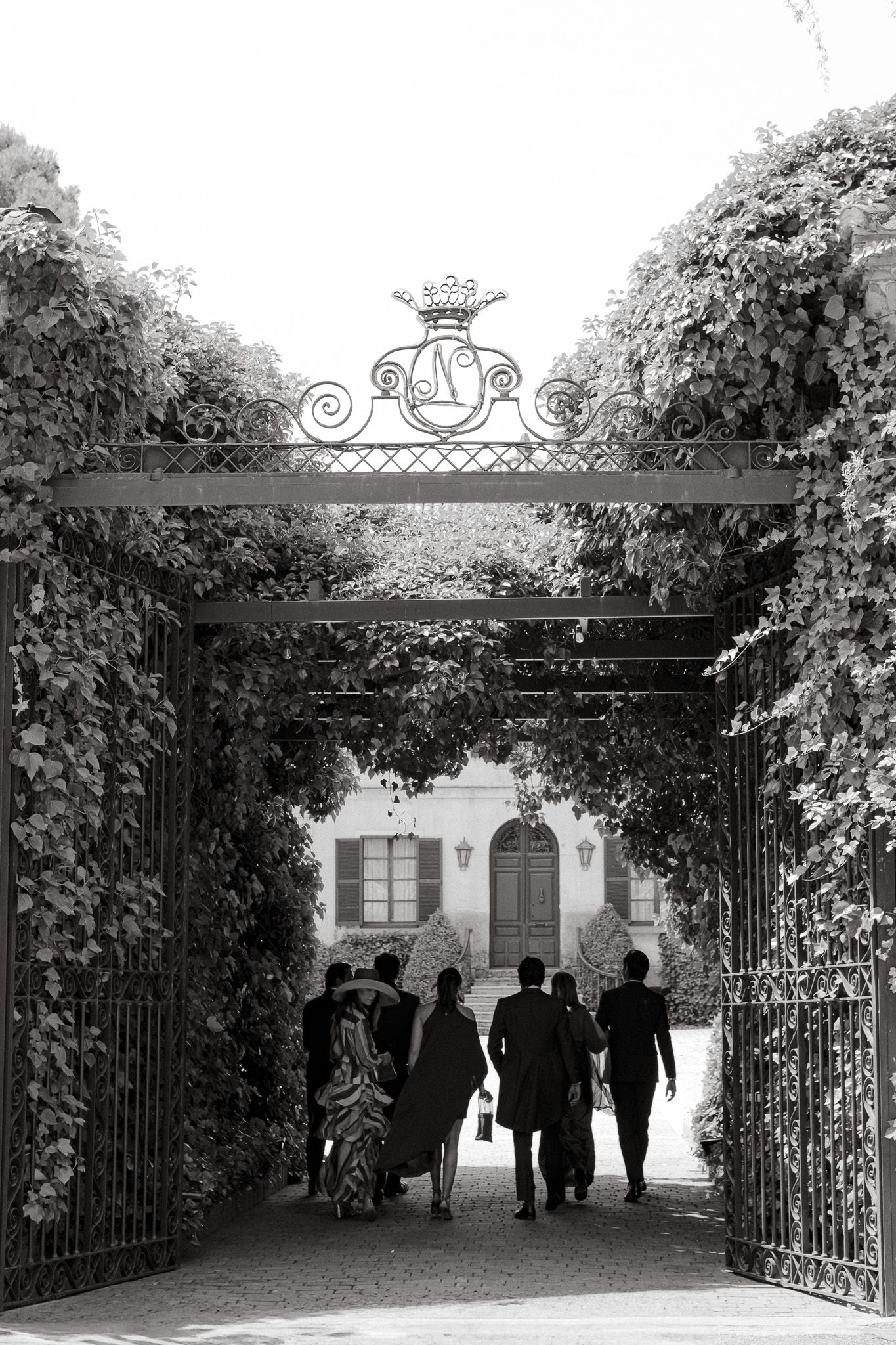 Guests walk through an ornate garden archway entrance with decorative ironwork and lush greenery.