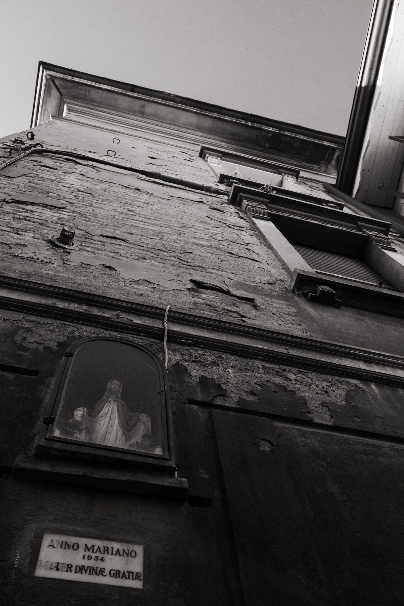 Low angle view of weathered building exterior with window and religious statue.