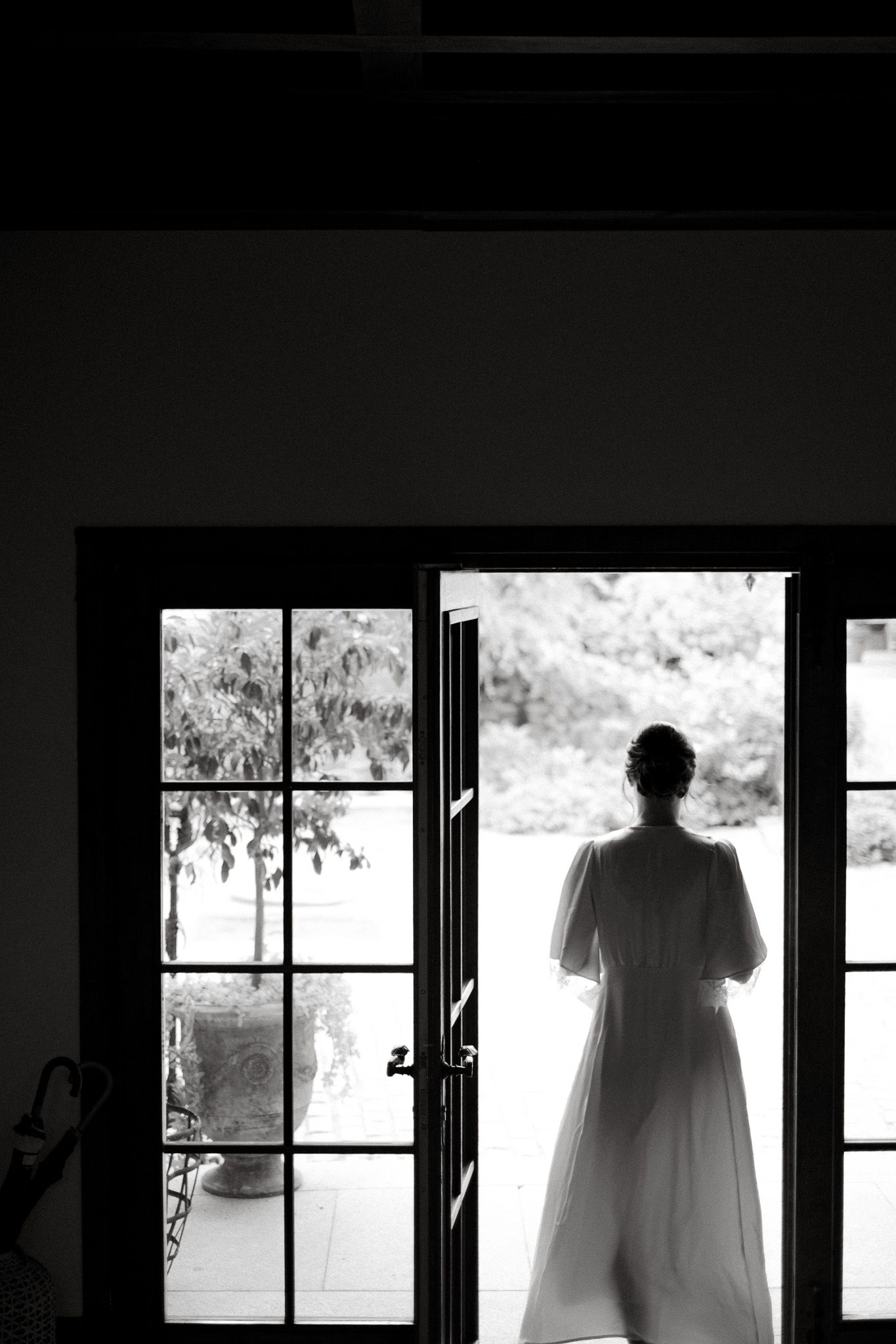Silhouette of person in white dress standing in doorway framed by French windows.