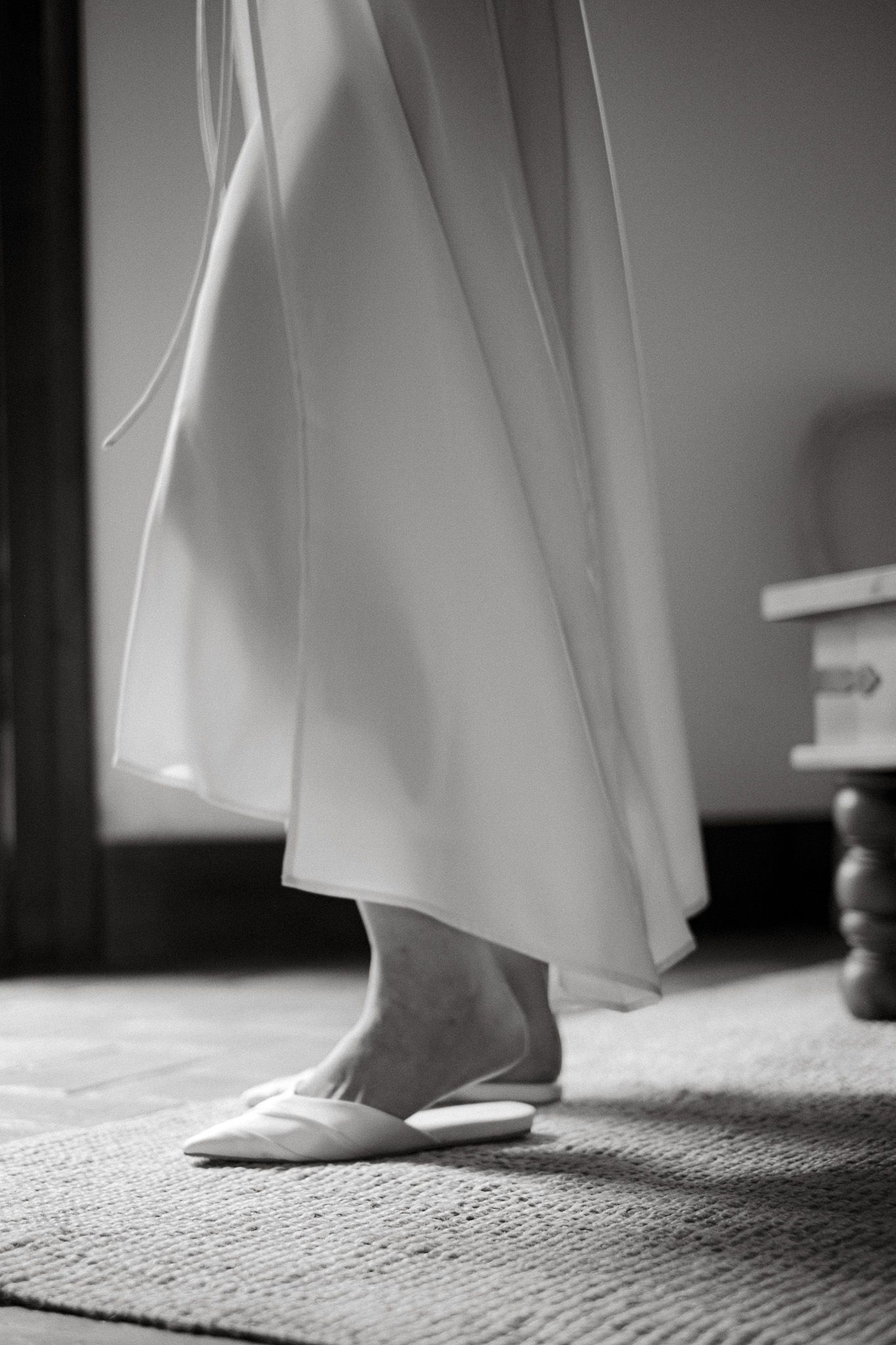 Close-up of a bride's feet in ballet flats beneath flowing white dress hem.