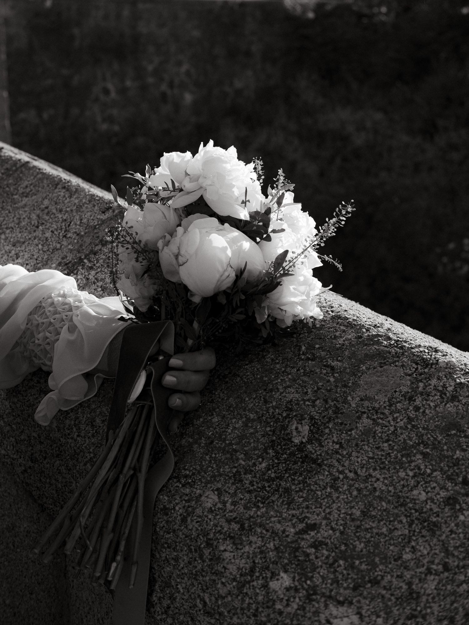 Black and white image of a delicate peony bouquet resting on a stone surface.