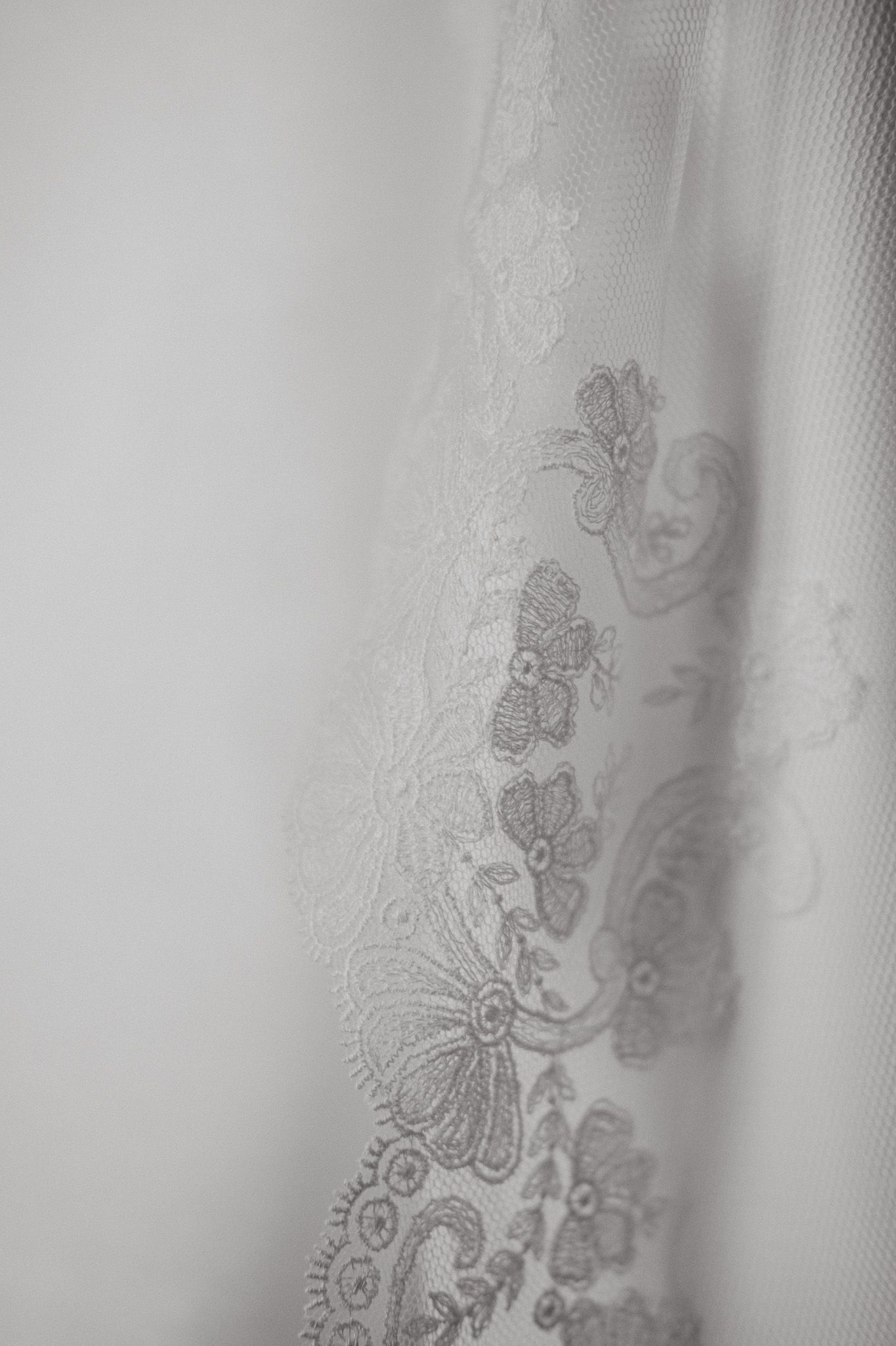 Delicate lace embroidery detail with floral patterns and swirls on white fabric in soft focus.