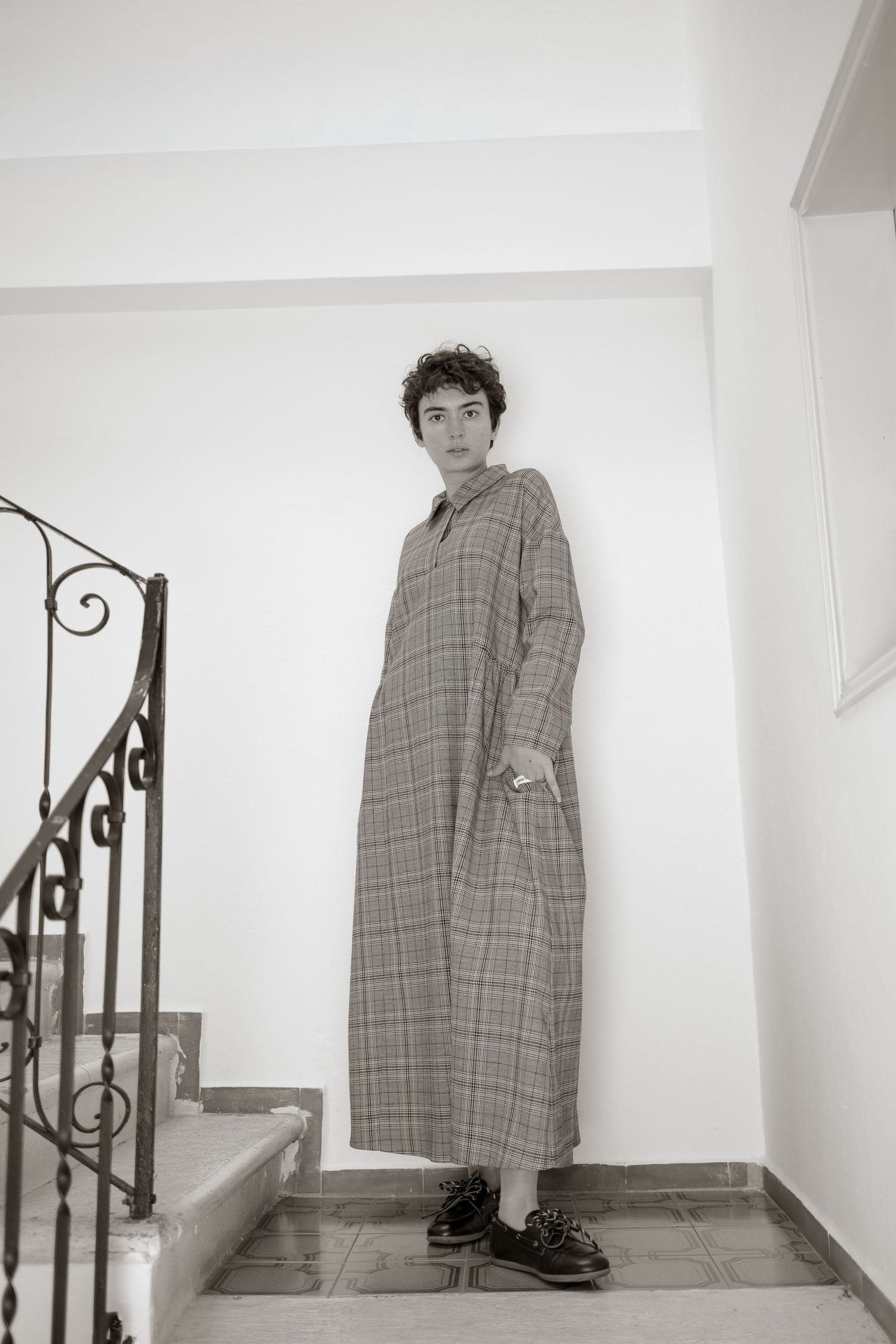 A sequence of four black and white photos showing someone in a plaid coat standing near a staircase railing.