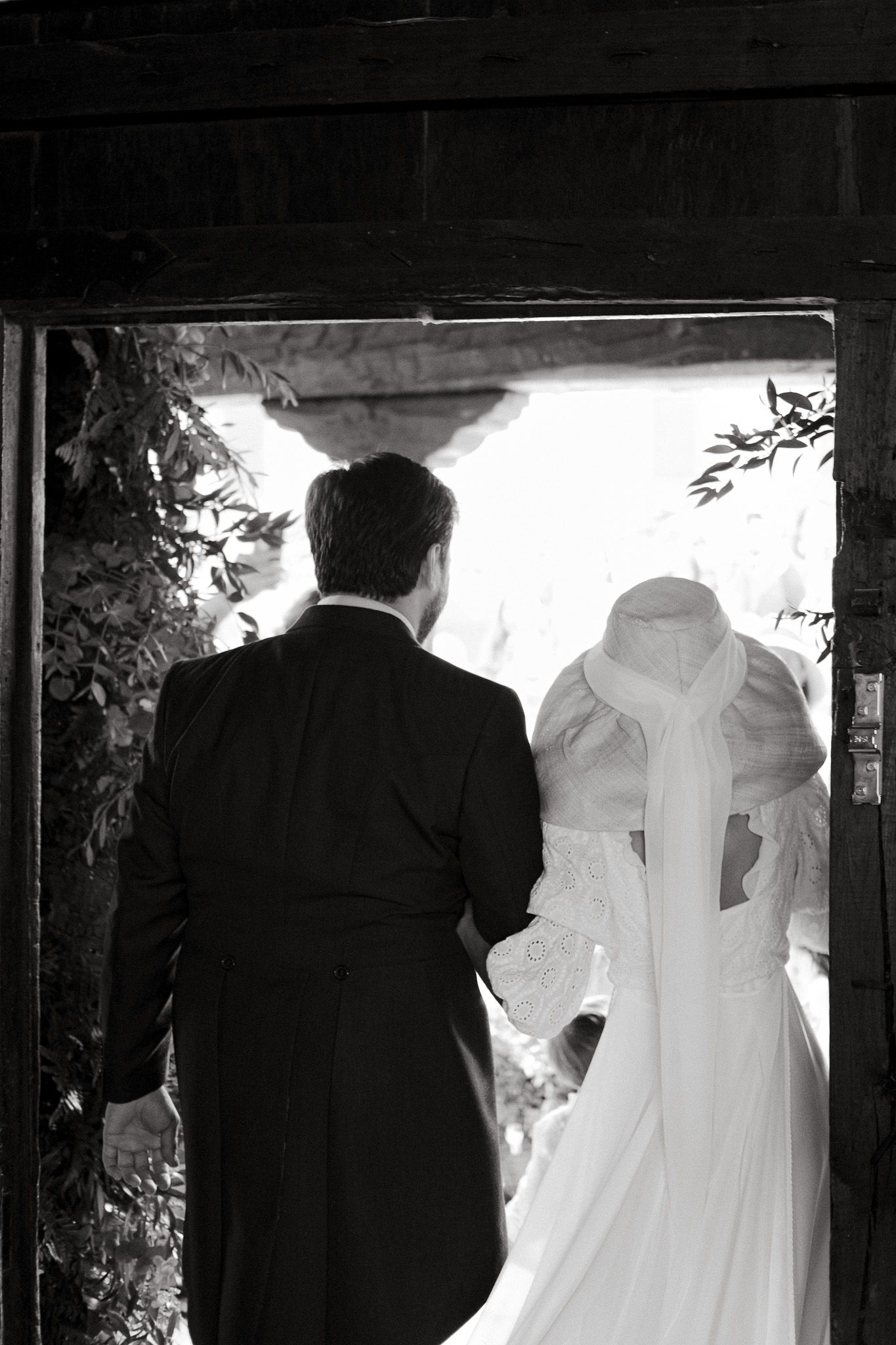A couple in wedding attire stand silhouetted in a doorway on their wedding day.