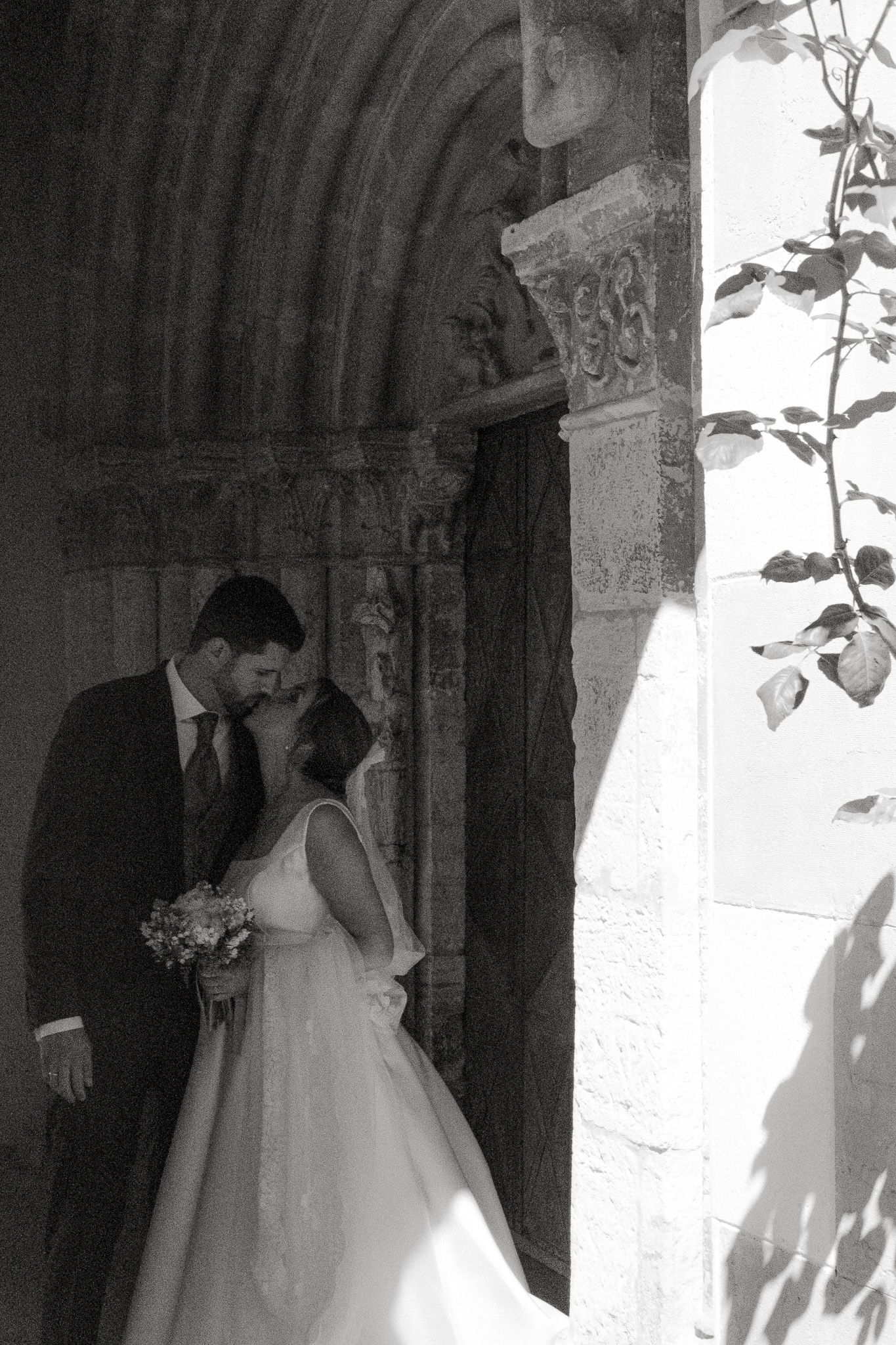 A tender black and white moment between newlyweds standing in an ornate stone archway.