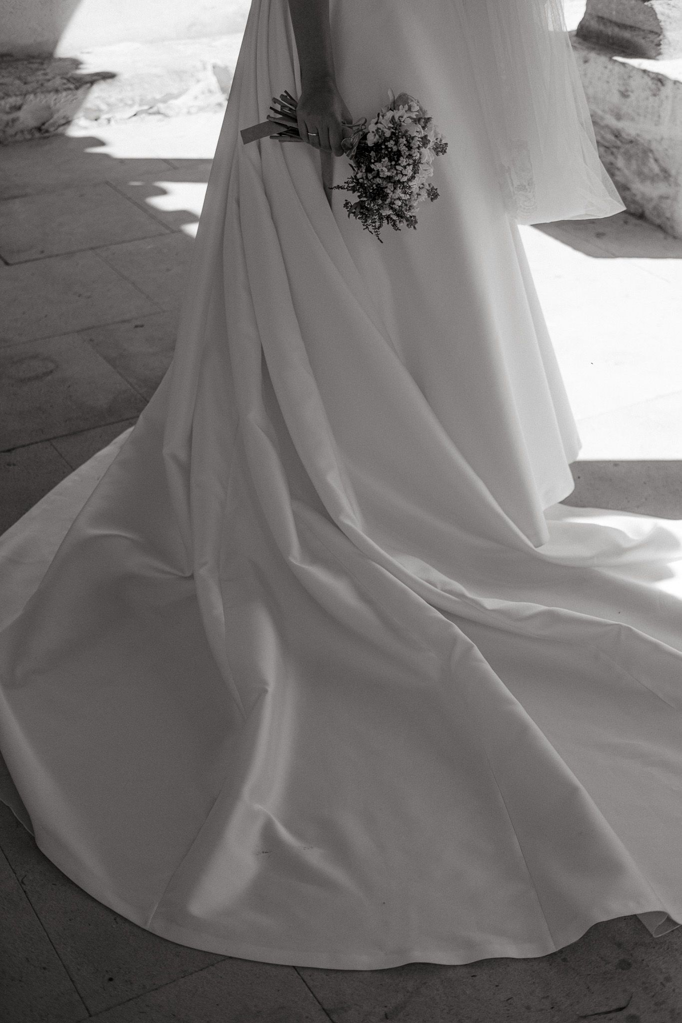 Flowing white wedding dress train with floral bouquet detail on stone floor.