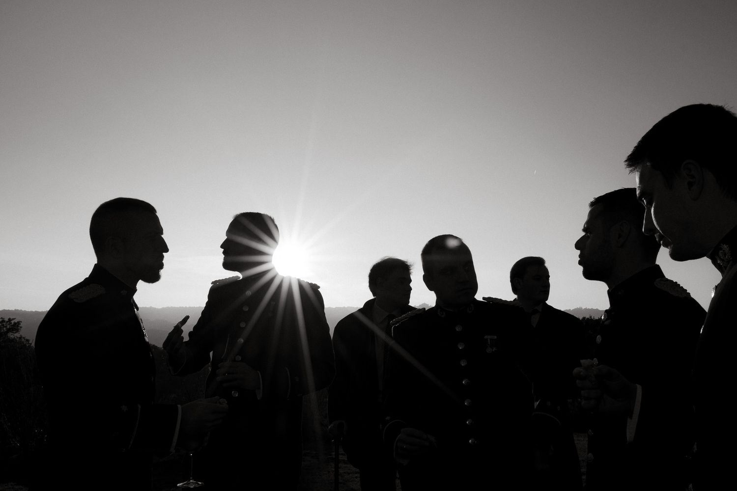 Silhouettes of people standing in a group with sun flare between them.