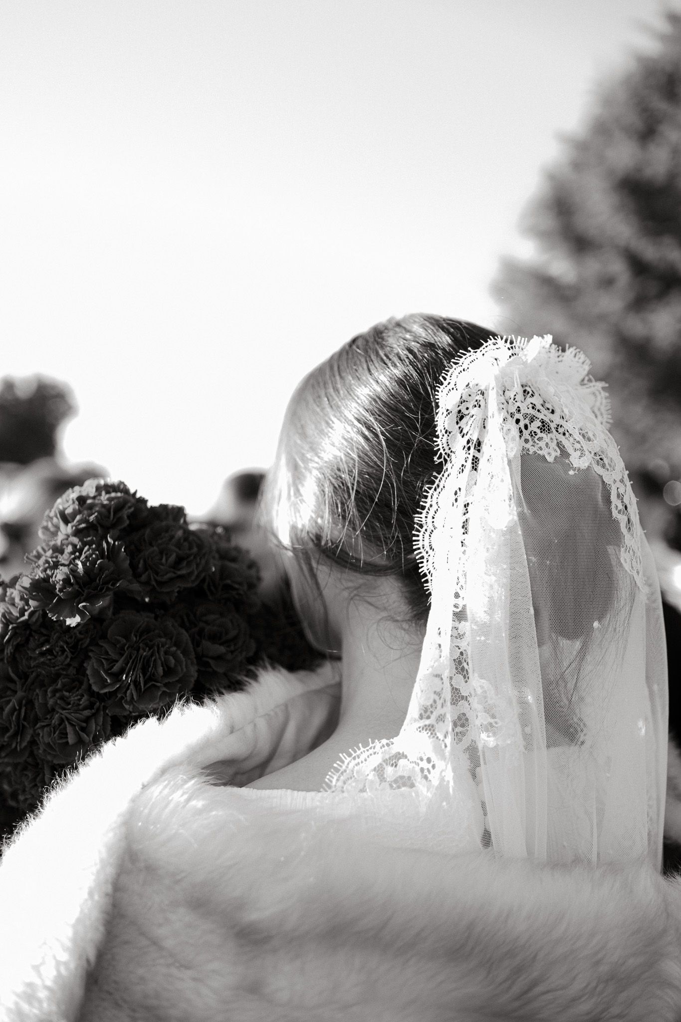 Bride wearing elegant lace veil and fur wrap shown from behind.
