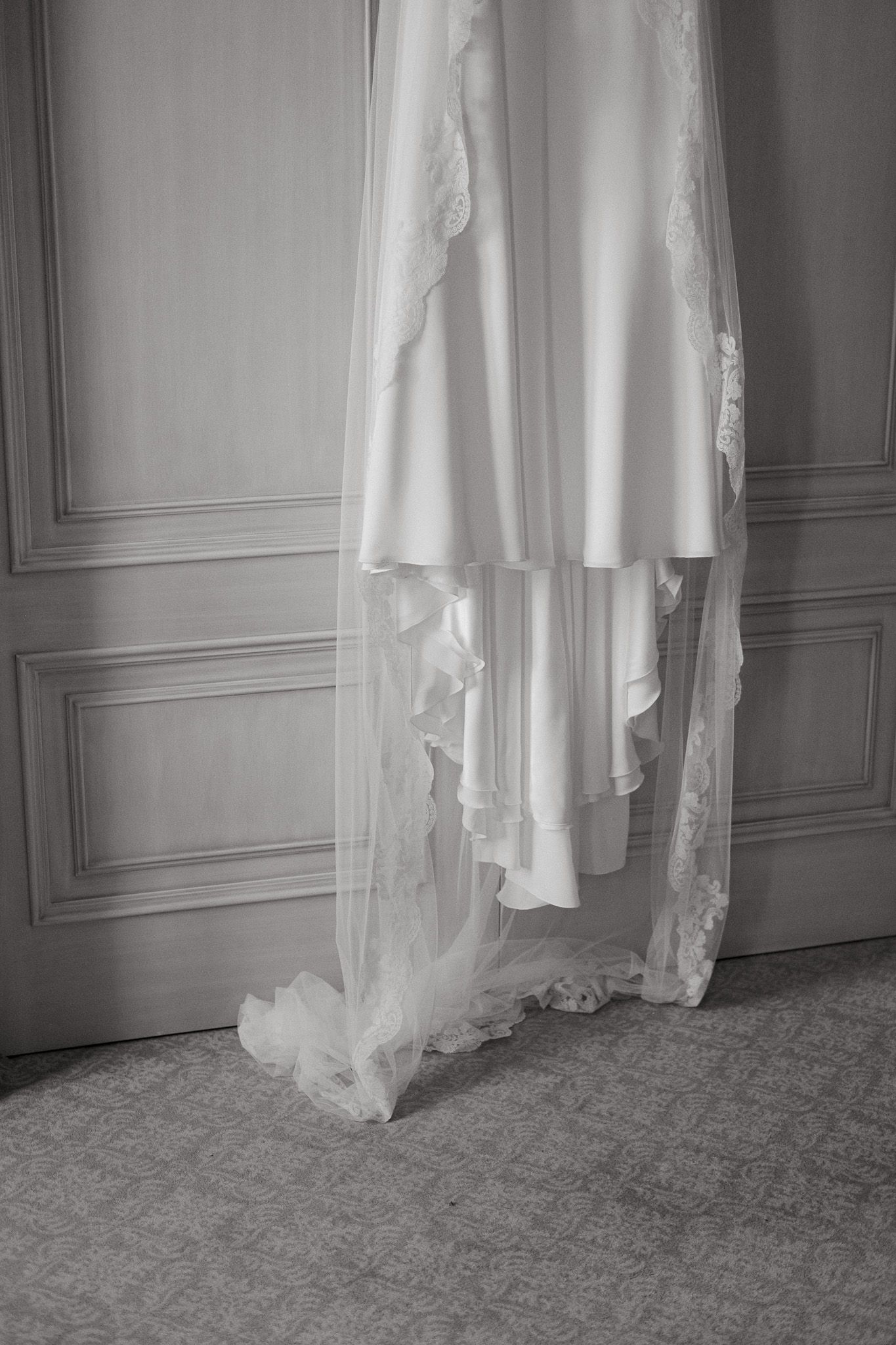 A delicate white wedding dress with lace details hanging against a paneled wall.