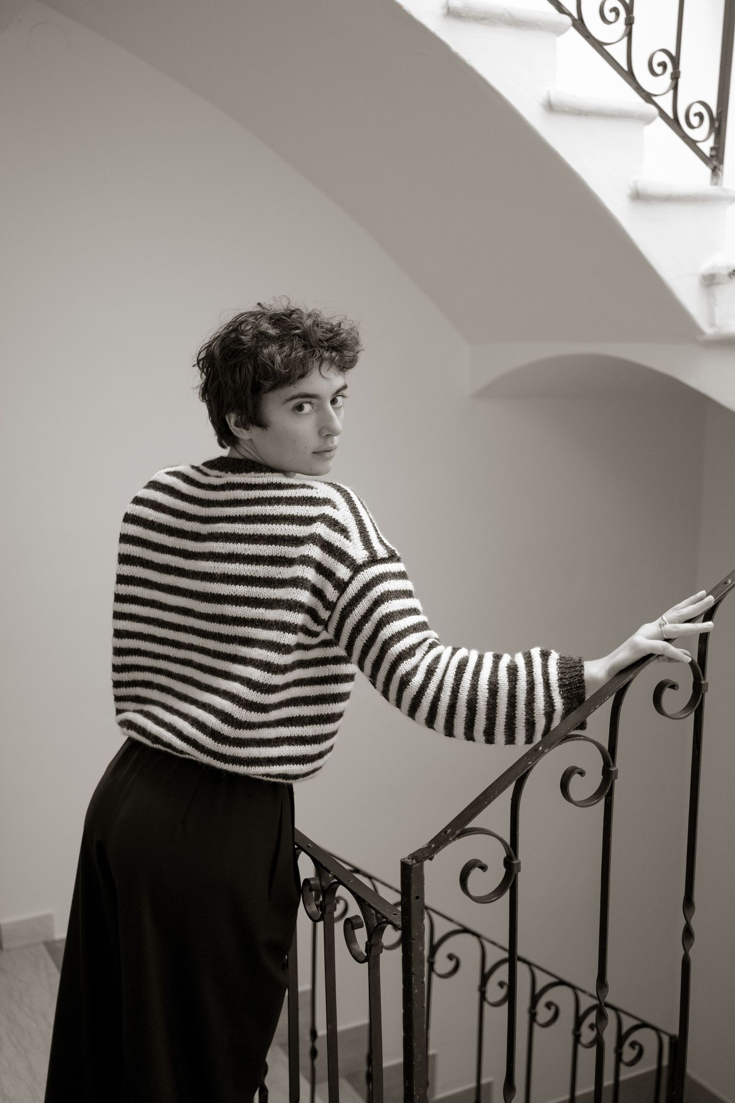 A person in a striped shirt and dark skirt stands on stairs in a dramatic black and white photo series.