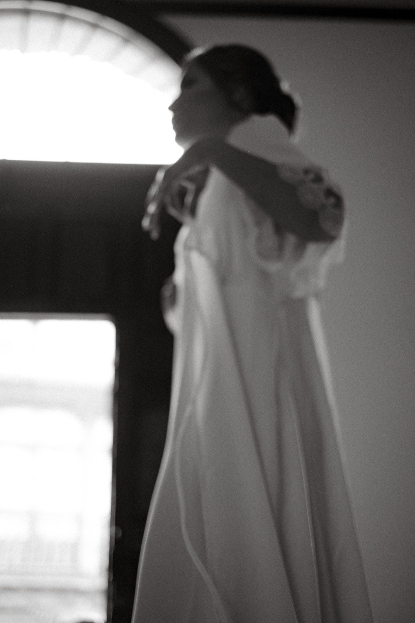 Silhouette of a bride in flowing white dress against backlit window.