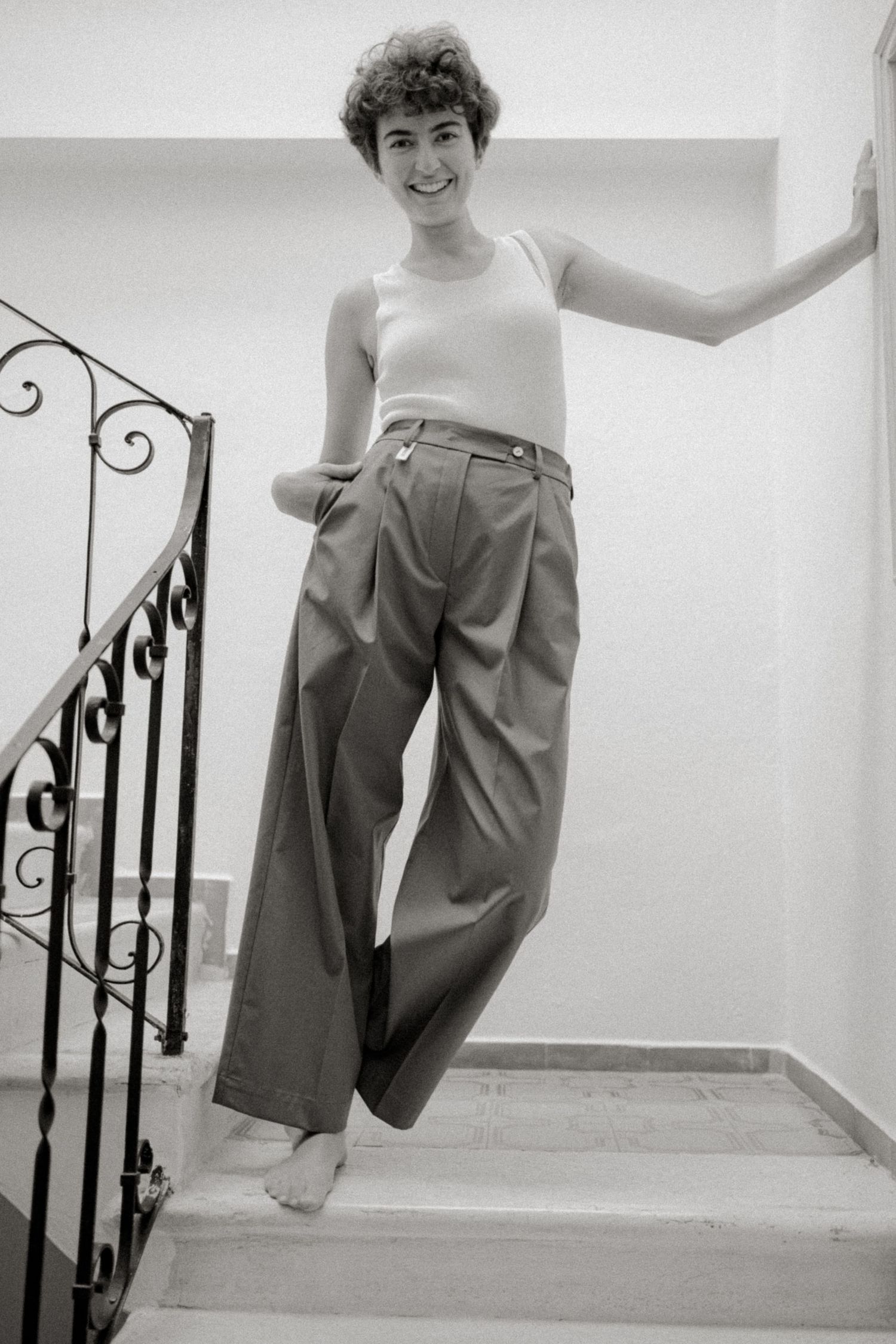 Black and white photo series showing someone posing playfully on white stairs with decorative iron railings.