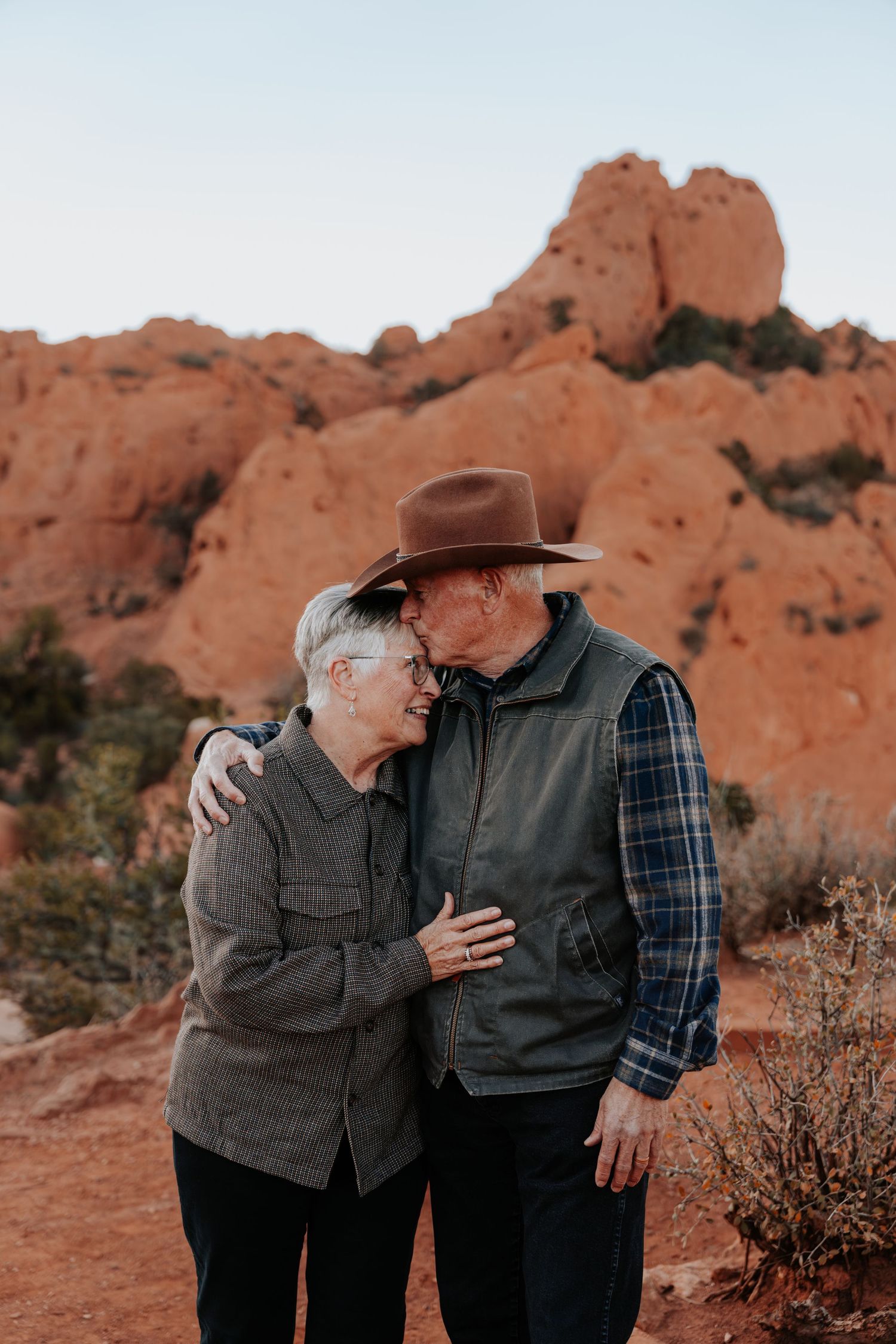 Elderly couple sharing a tender moment at Garden of the Gods with red rock formations behind them.