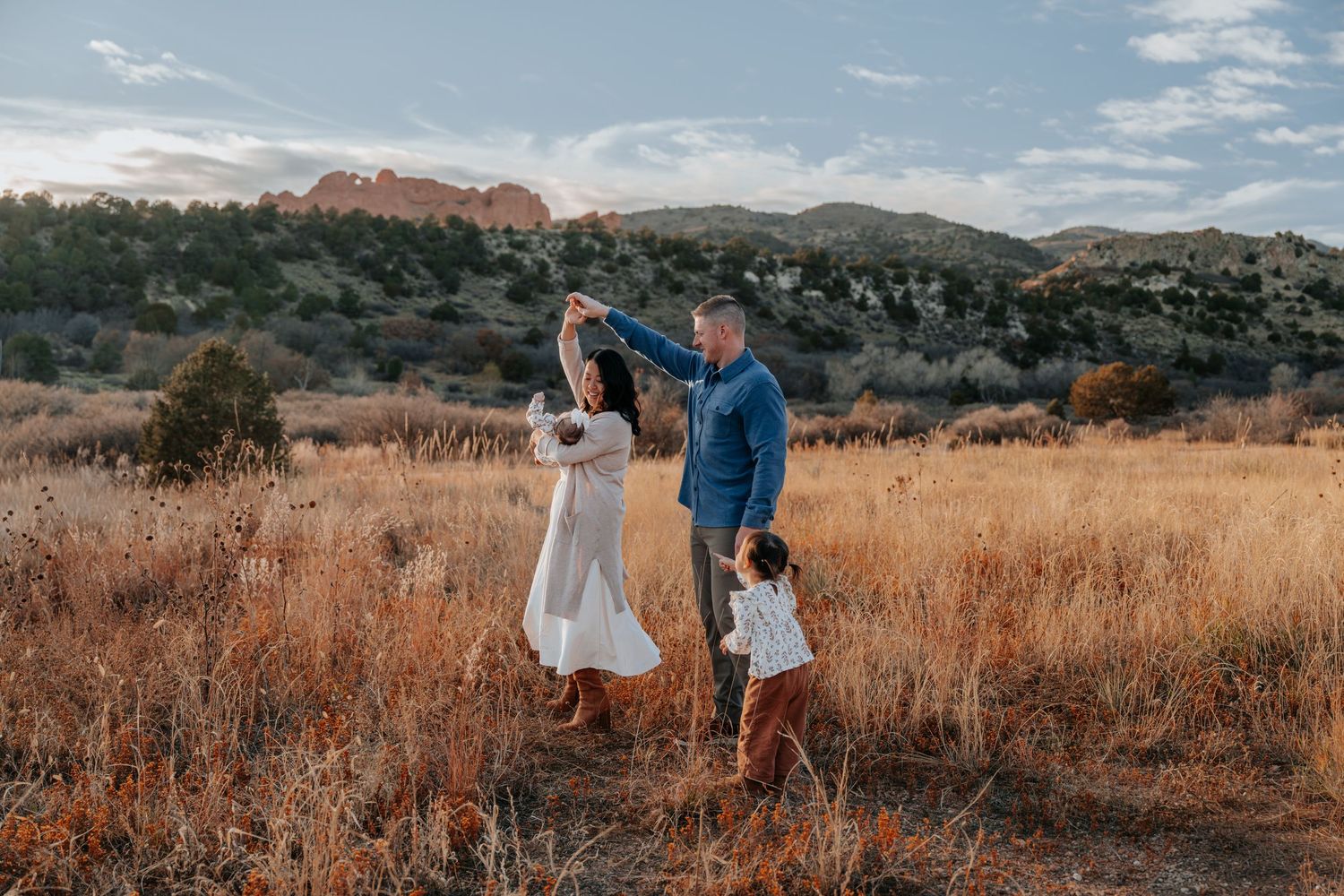 Family dancing and twirling in a golden meadow with red rock formations in background.