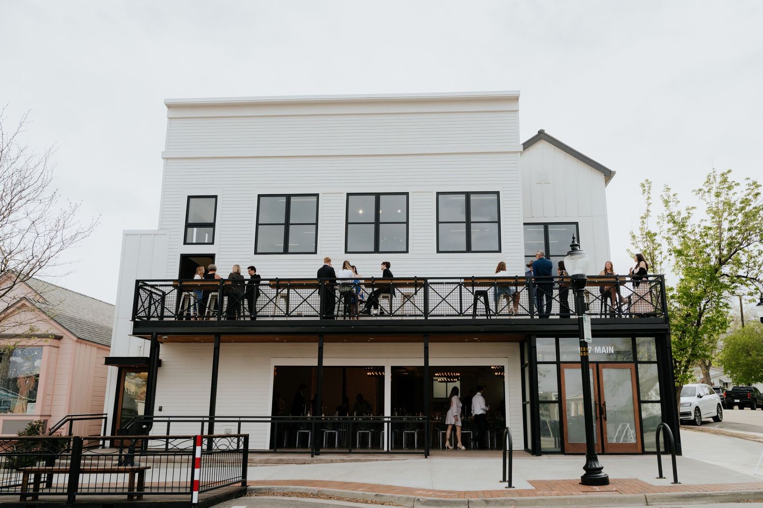 Guests gathering on black iron balcony of modern white two-story wedding venue building.
