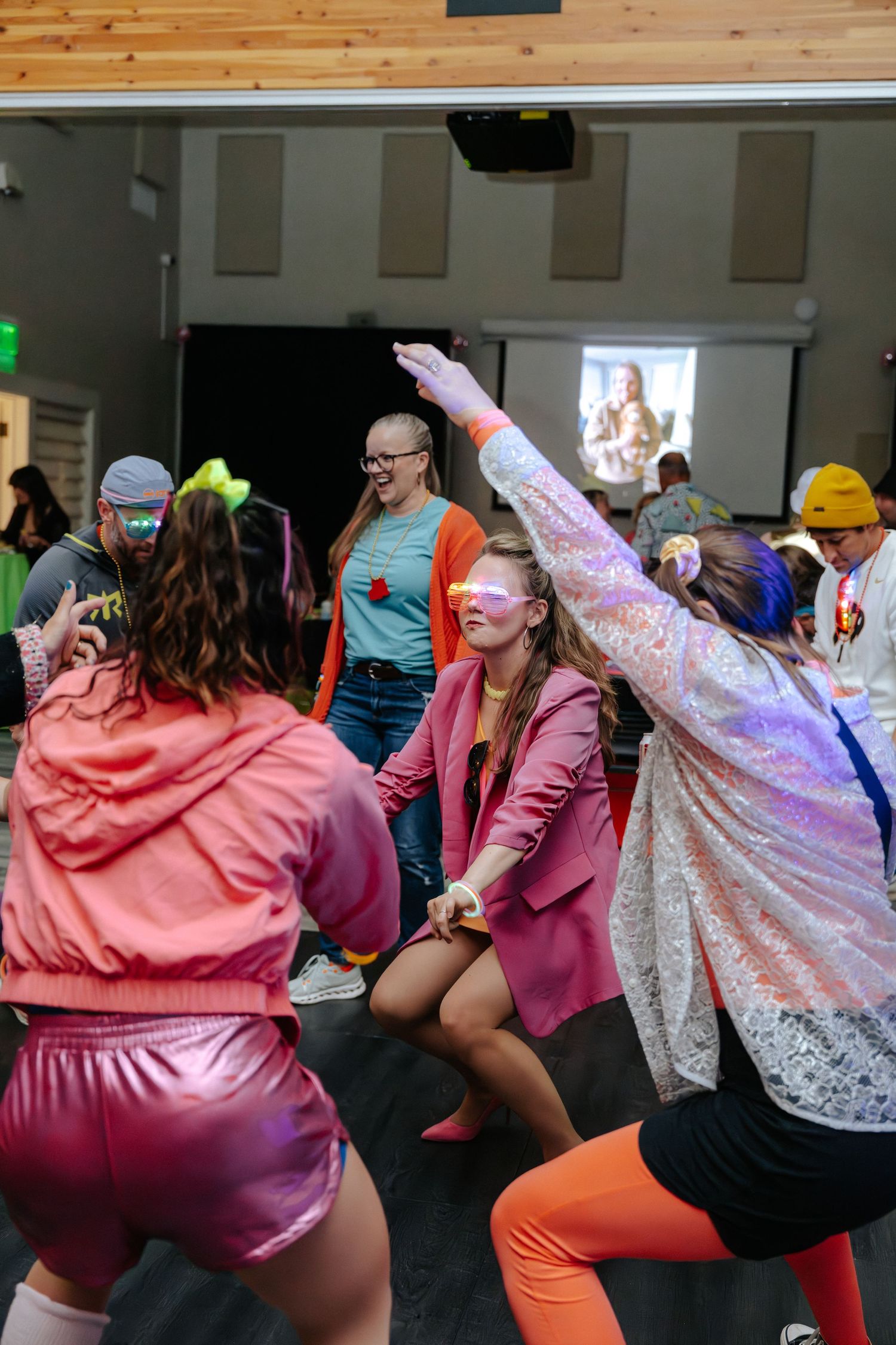 Group of people in colorful 80s-themed outfits dancing and having fun at a vibrant indoor party event.