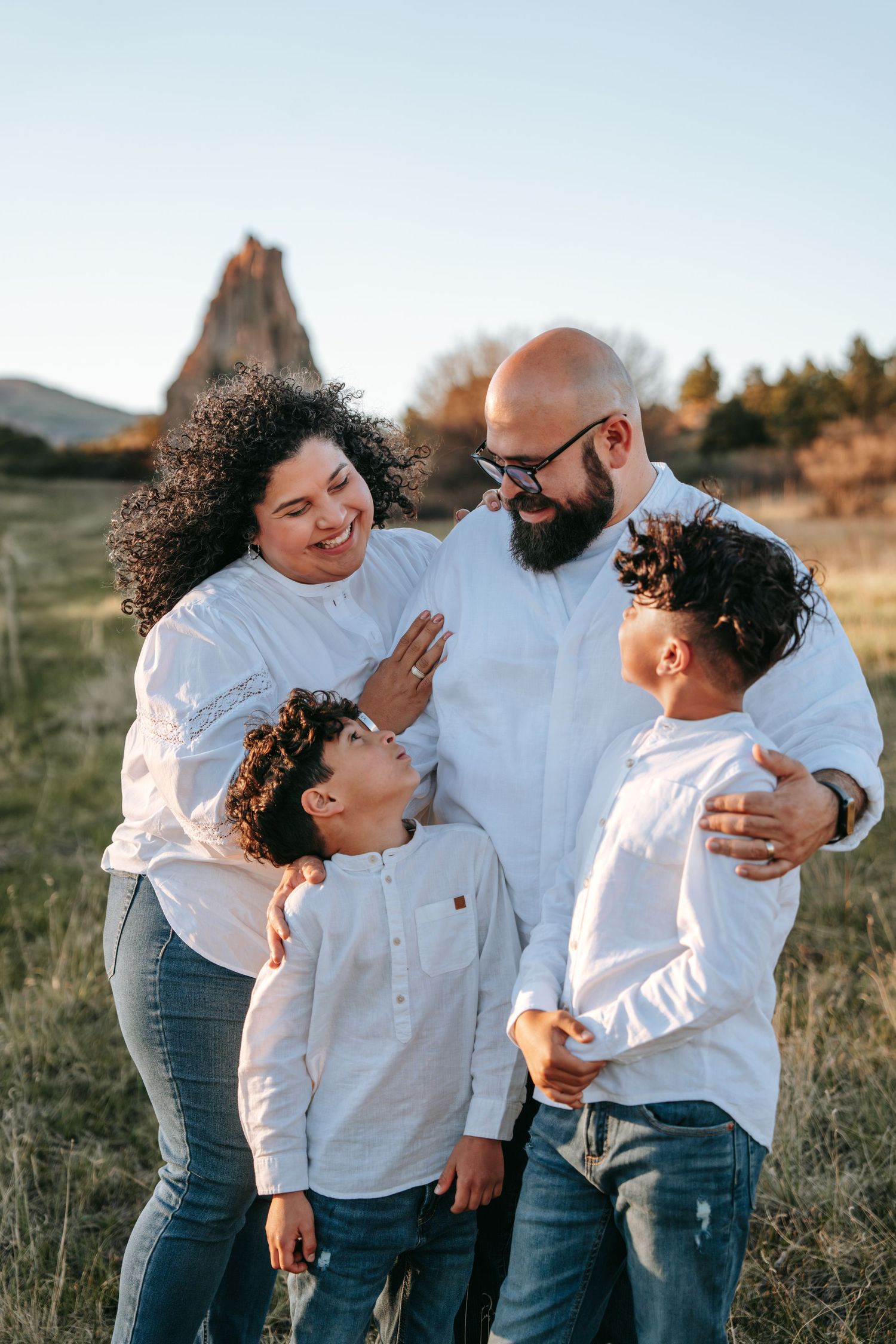 Joyful family of four in white shirts sharing a loving moment together in a sunlit grassy field.