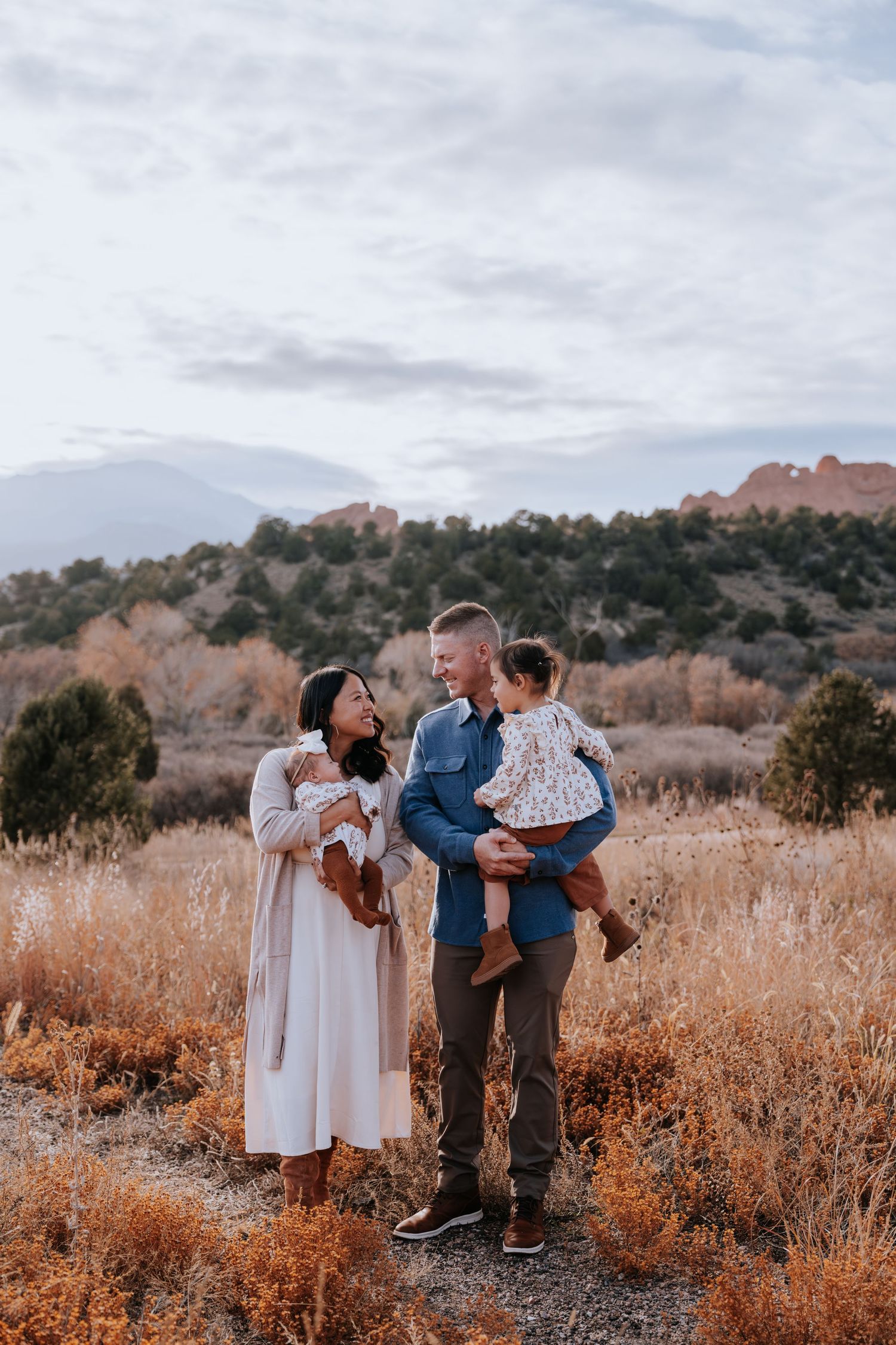 Happy family of four posing in autumn field with mountain and rock formations behind them.