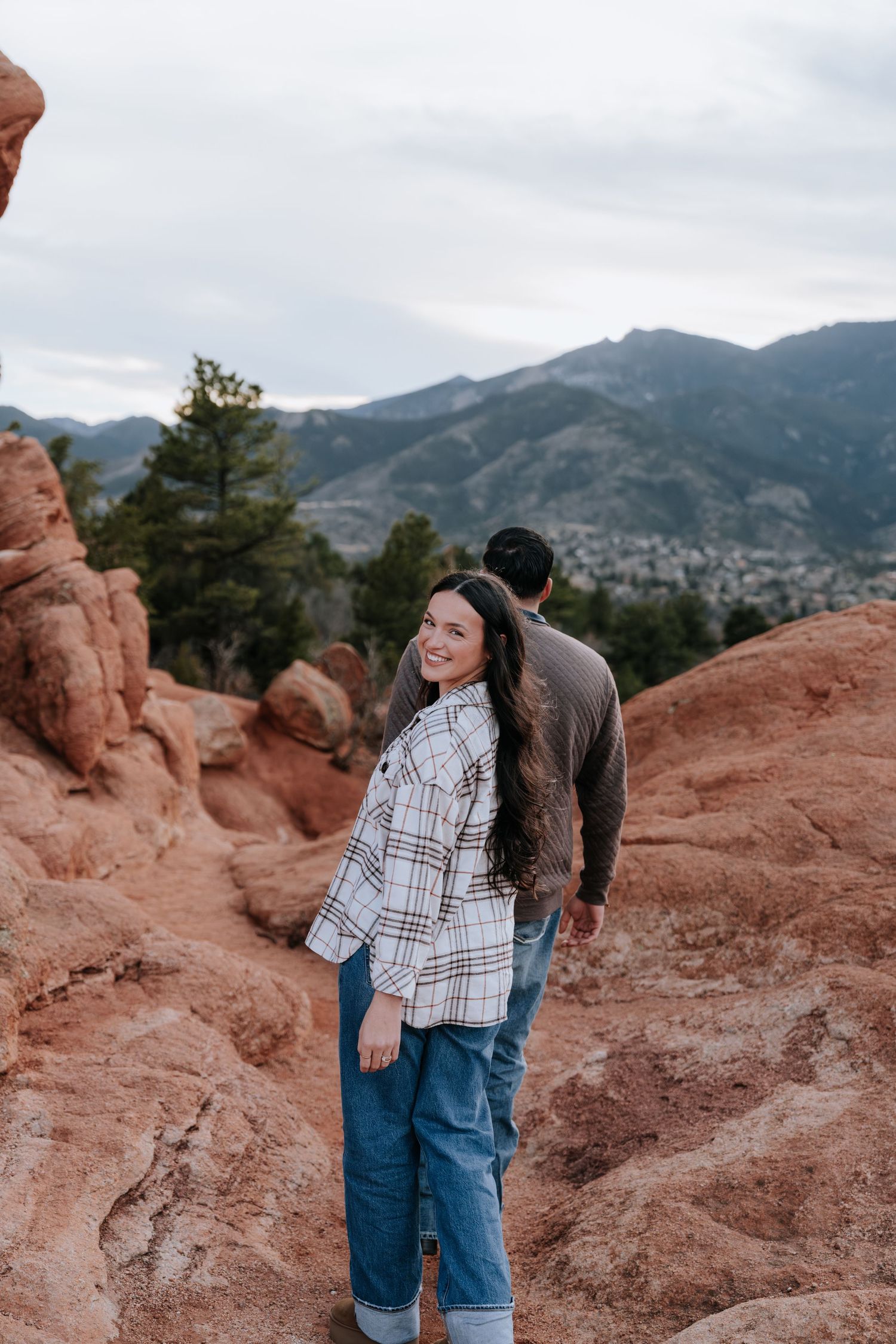 Smiling woman in plaid shirt poses with partner among red rock formations at Garden of the Gods.