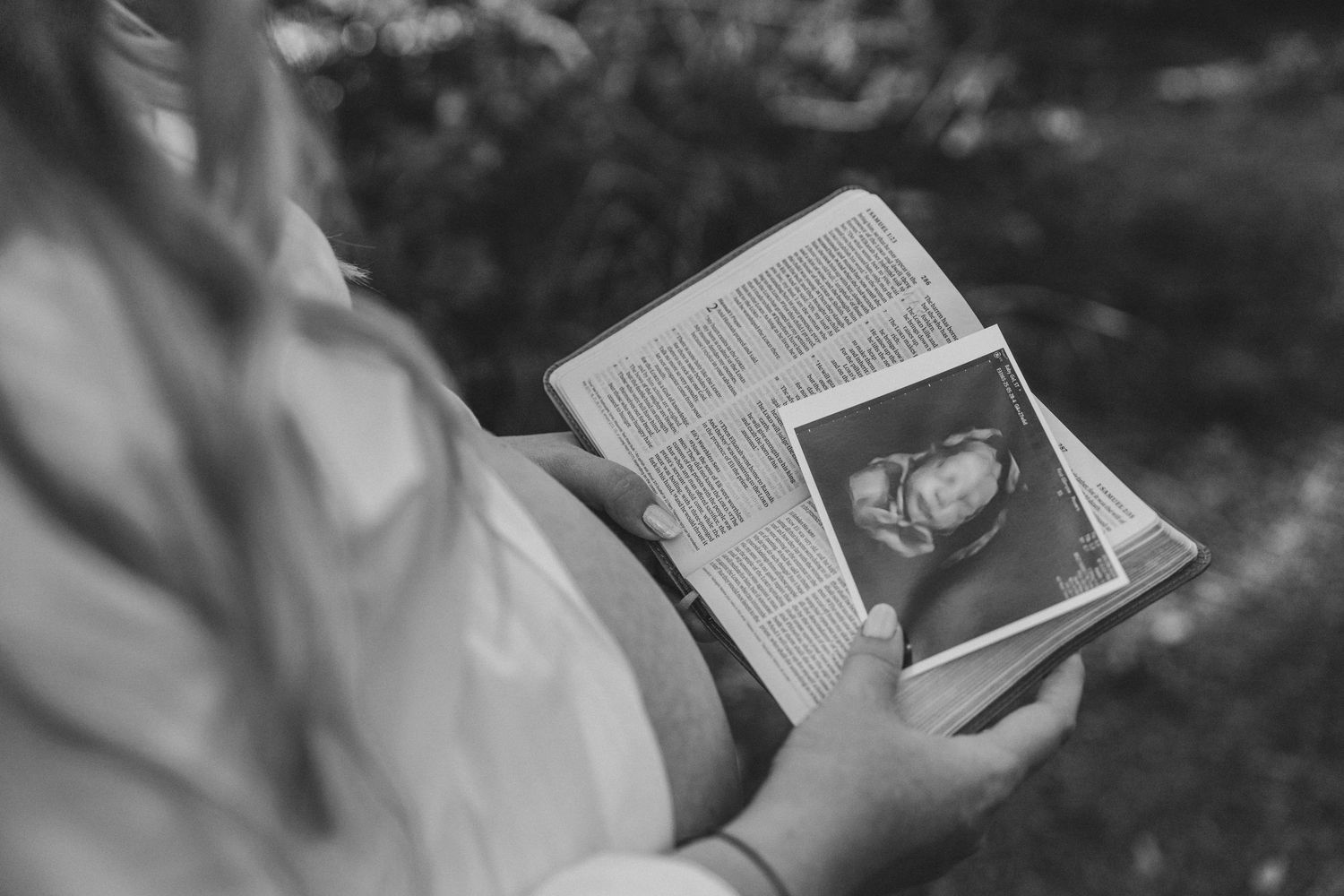 Black and white photo of pregnant woman holding ultrasound image over open book.