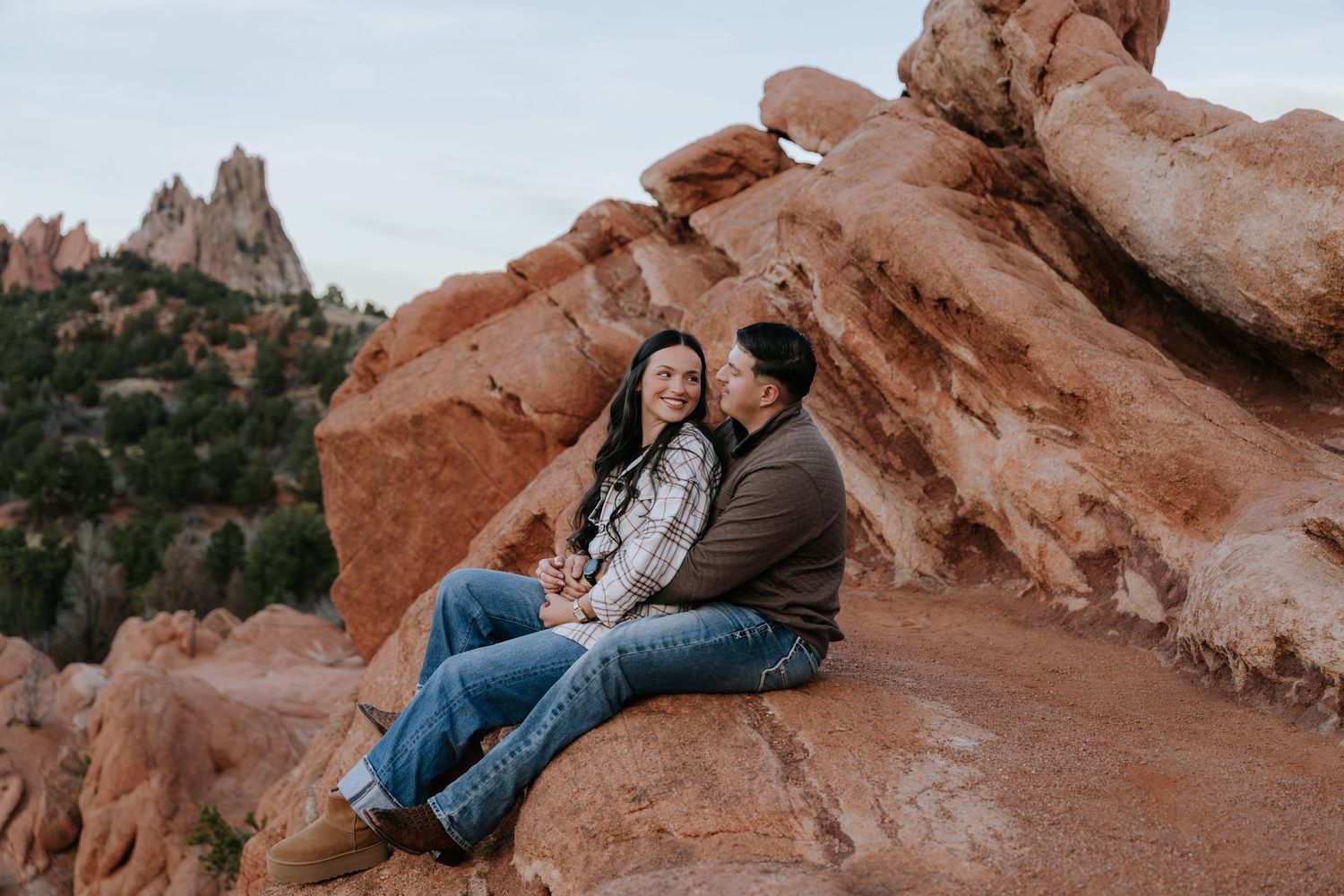 Couple sitting closely together on red rocks at Garden of the Gods with mountain views behind them.