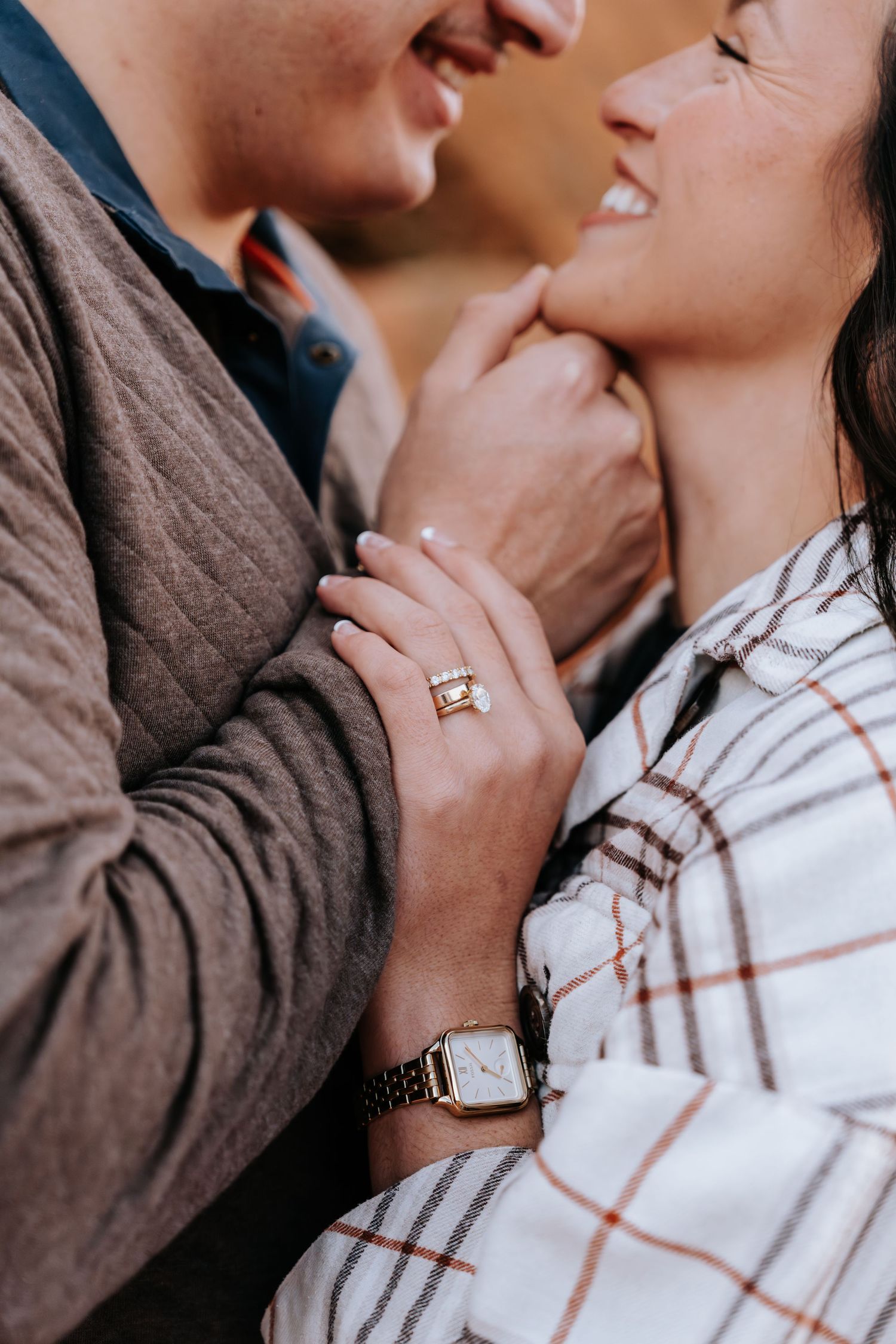 Close-up of couple nearly kissing showing womans emerald cut engagement ring and gold watch detail.