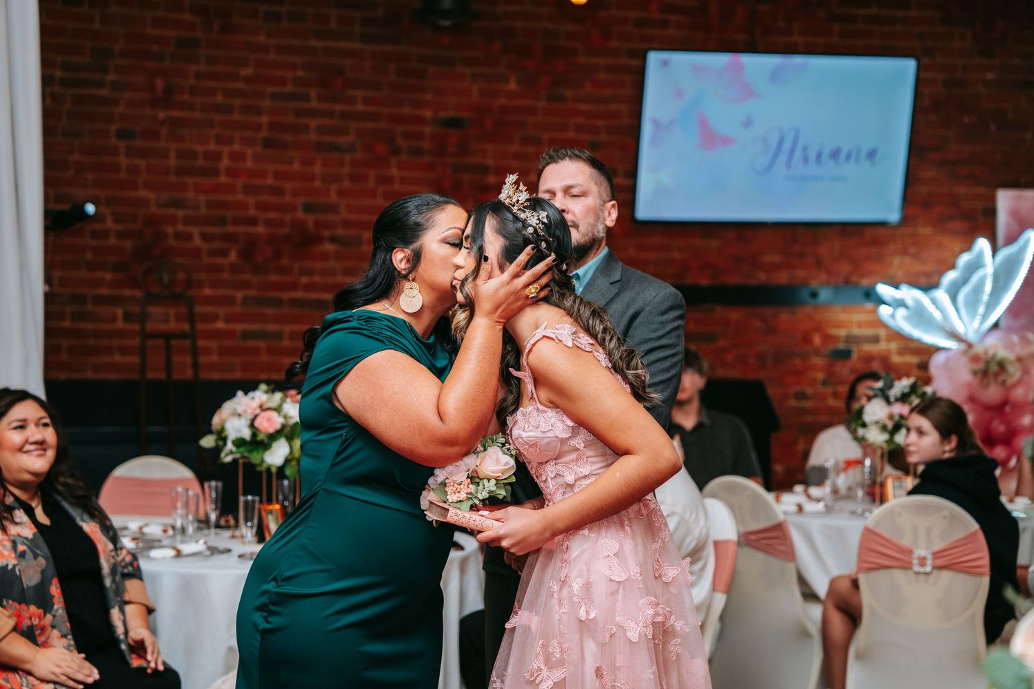 Parents placing tiara crown on quinceañera girl in pink gown during traditional ceremony.