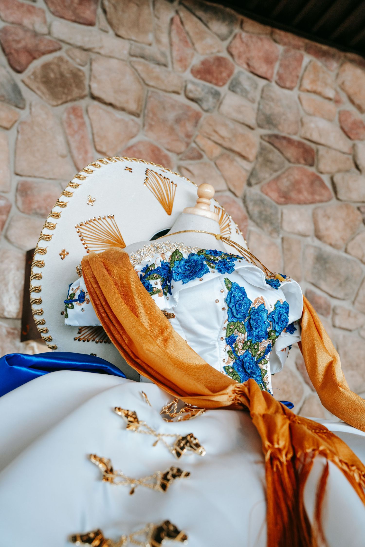 White and blue floral embroidered quinceañera dress with a sombrero and gold sash on display.