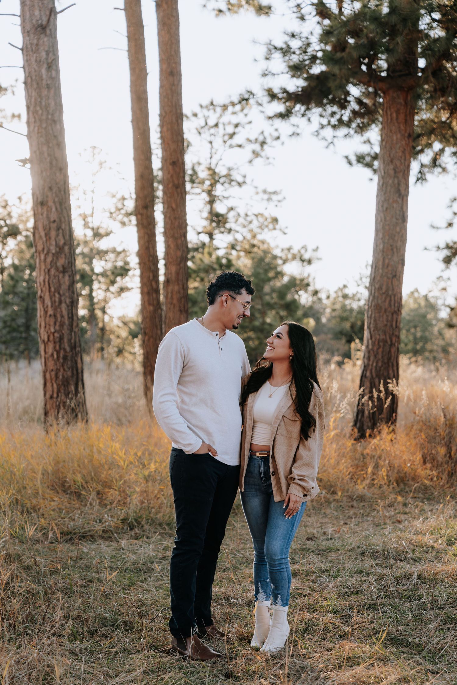 Couple sharing a tender moment standing together in a golden autumn forest field at sunset.