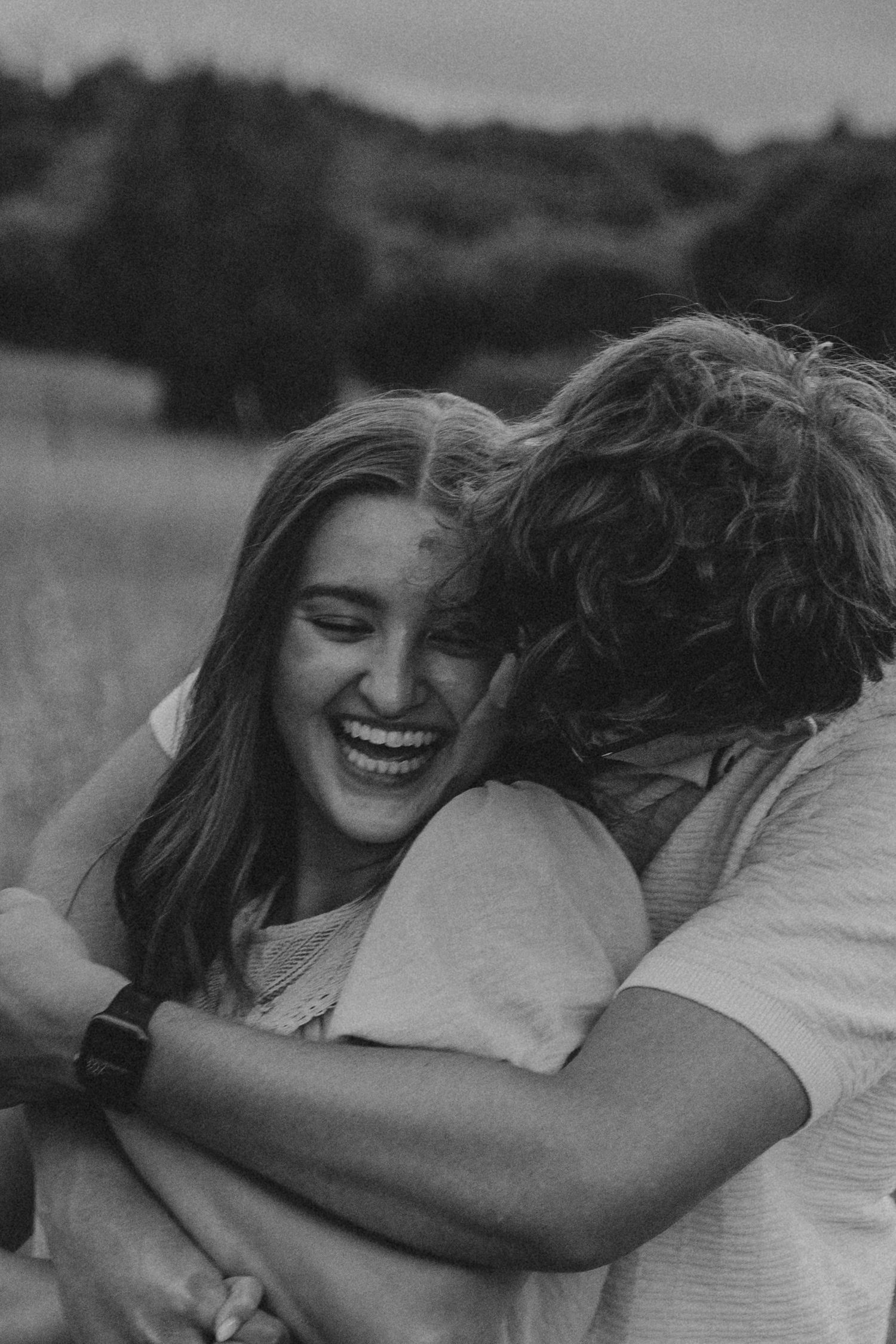 Black and white close-up of woman laughing joyfully while embracing her partner in a field.