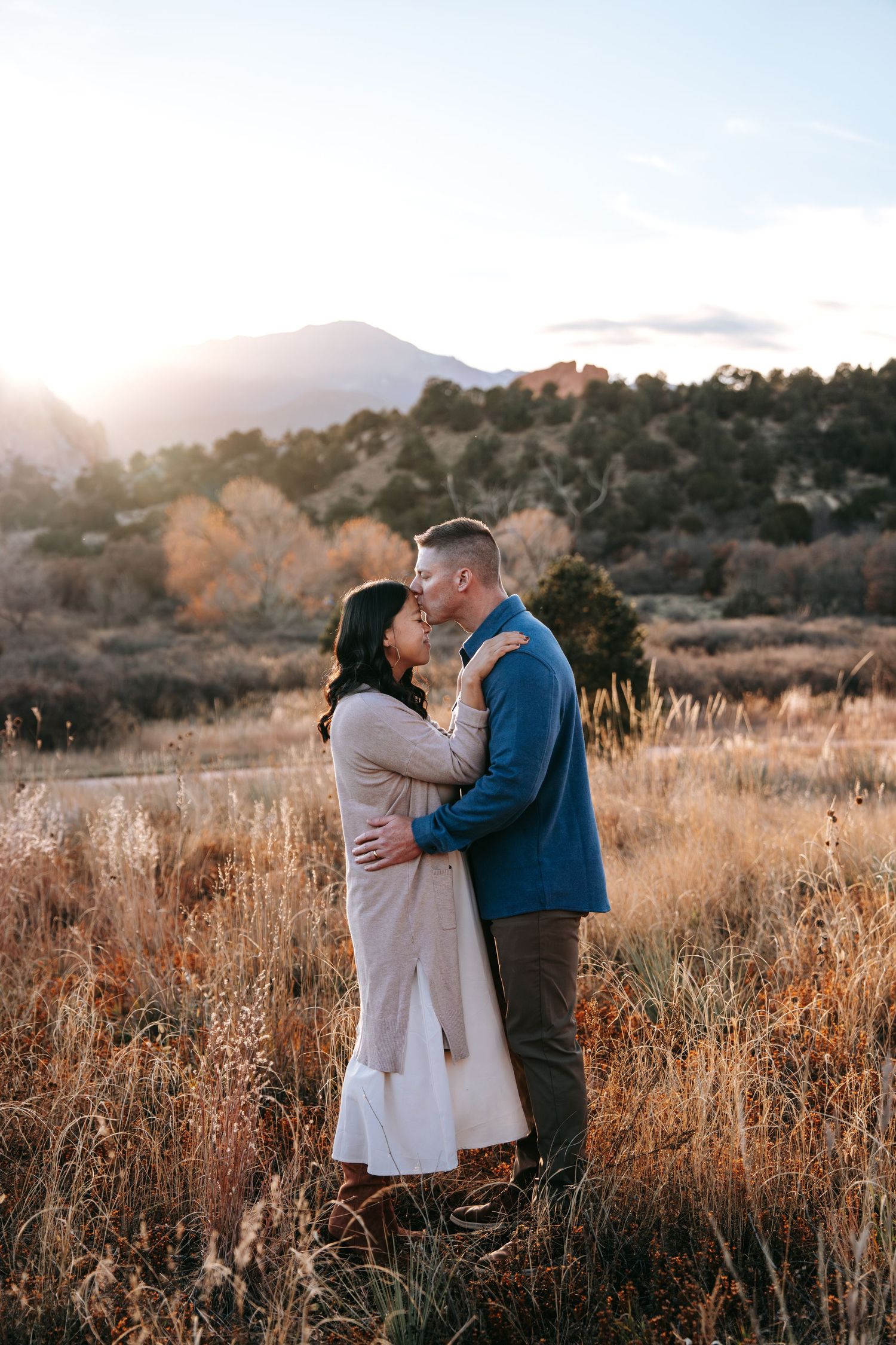 Couple sharing a romantic moment in golden autumn field with mountain backdrop at sunset.