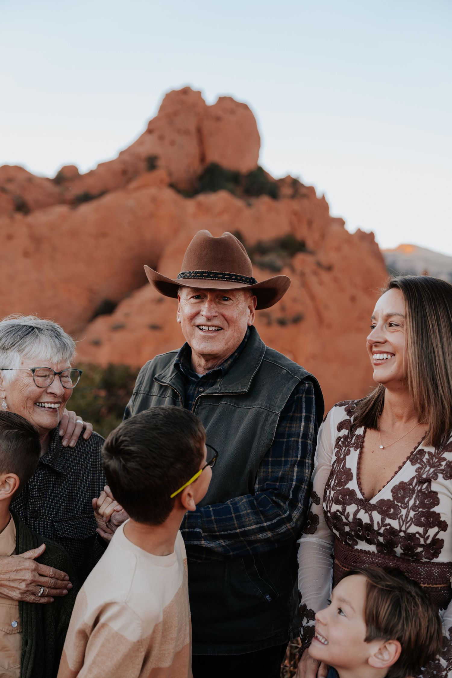 Multigenerational family sharing a joyful moment outdoors with glowing red rock formations at sunset behind them.