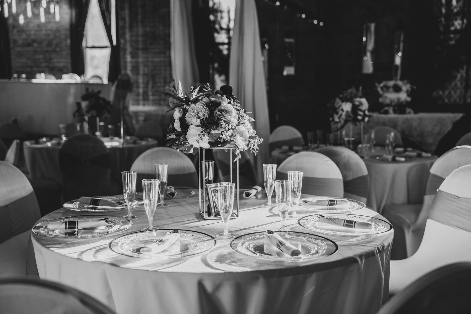 Black and white photo of an elegant round reception table with tall floral centerpiece and formal place settings.