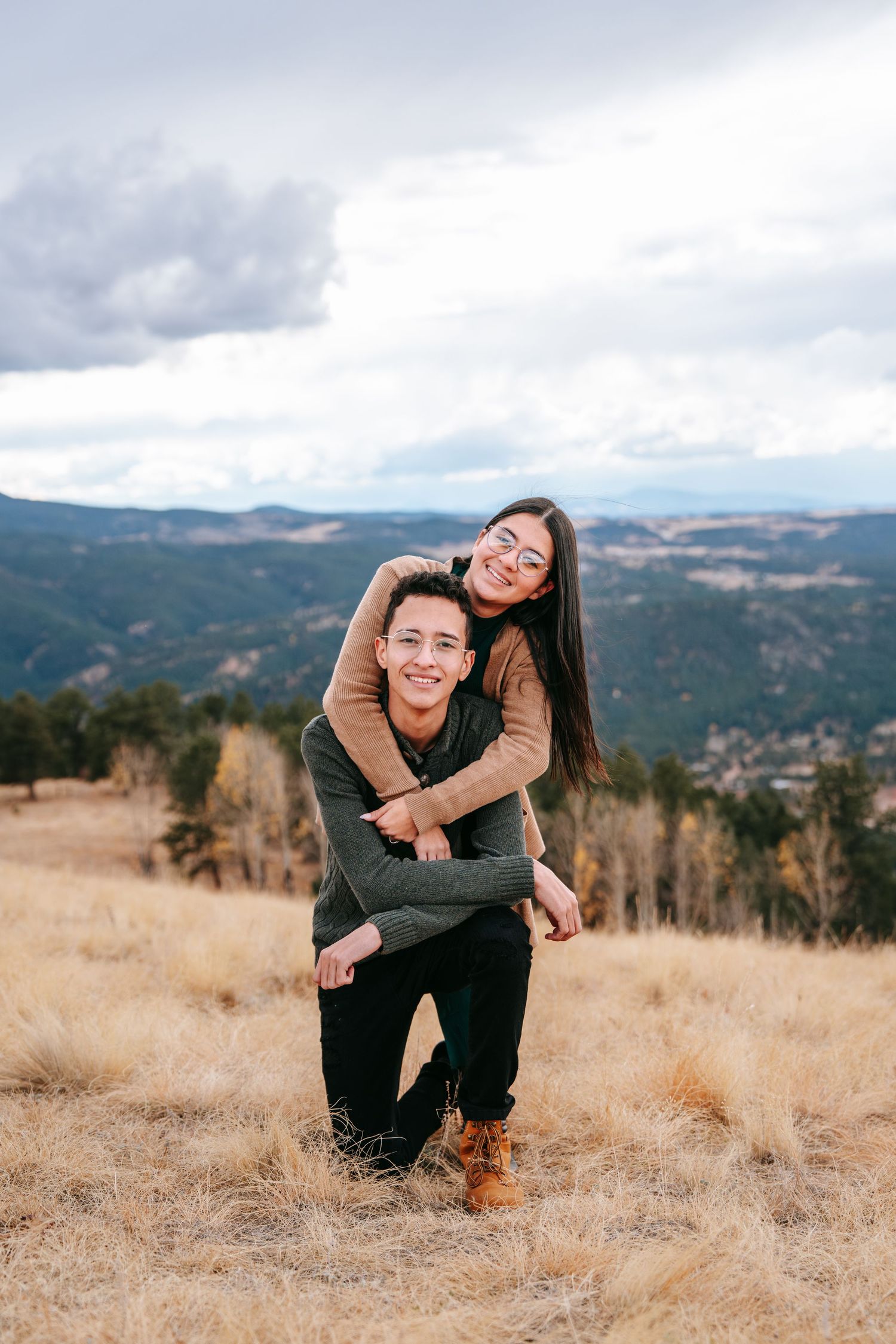 Young woman giving a piggyback ride to a smiling man in a golden autumn mountain meadow.