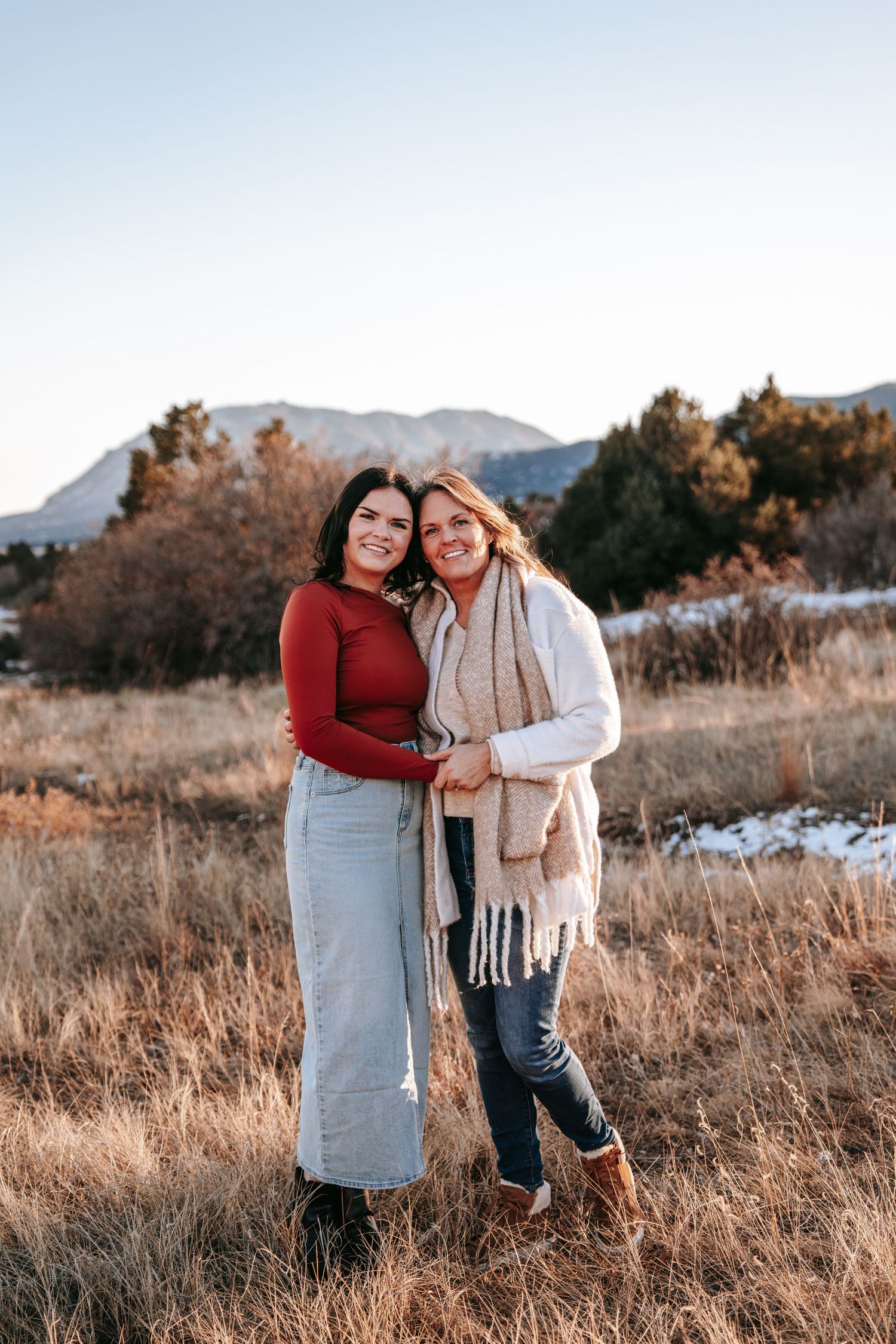 Mother and daughter smiling together in cozy fall outfits with mountain backdrop in Colorado.