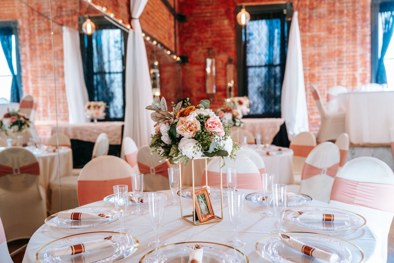Elegant wedding reception venue with round tables, pink floral centerpieces, and rose gold accents.