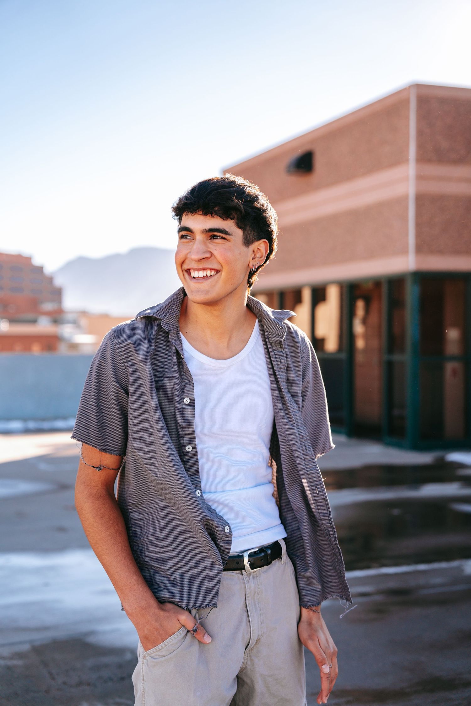 Smiling young man in gray shirt and white tee poses outdoors in golden sunlight.