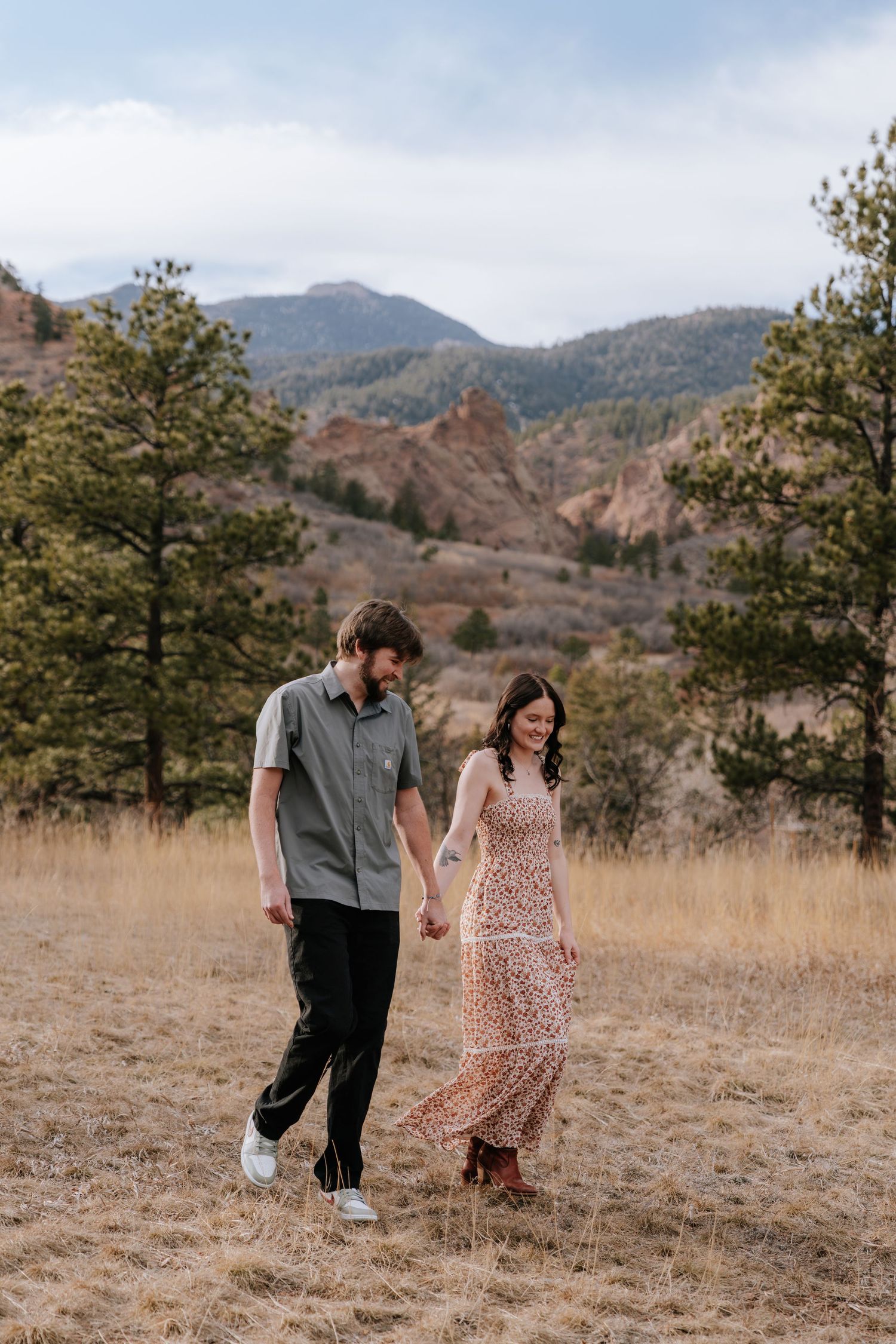 Couple holding hands walking through golden meadow with stunning Colorado mountain backdrop.