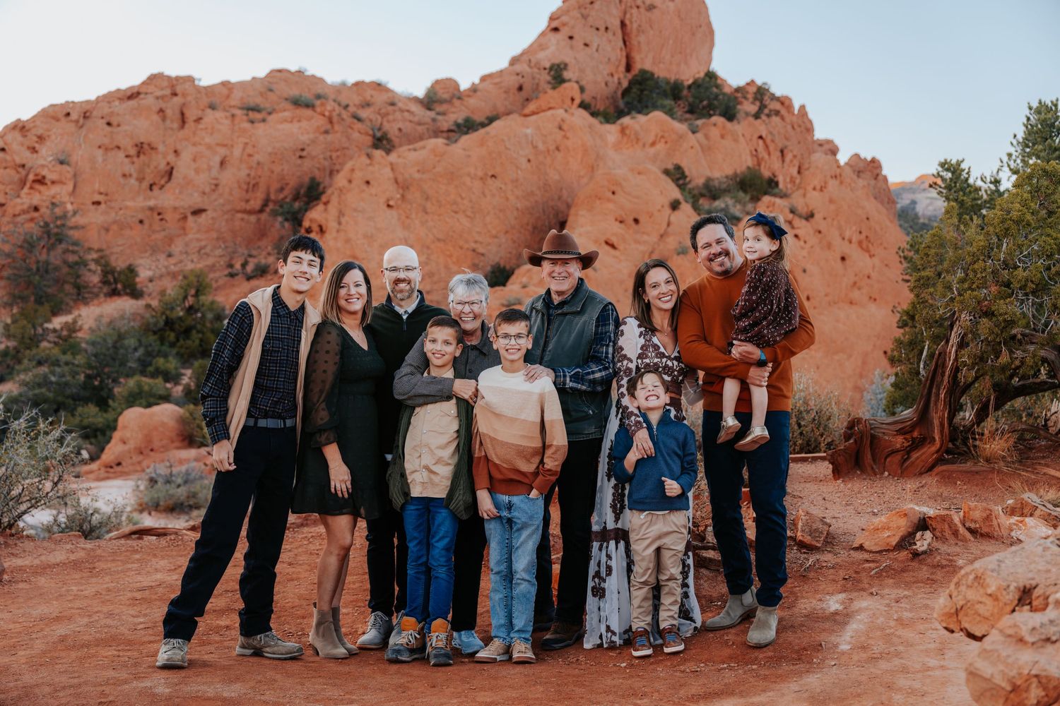 Large multigenerational family group posing together in front of dramatic red rock formations outdoors.