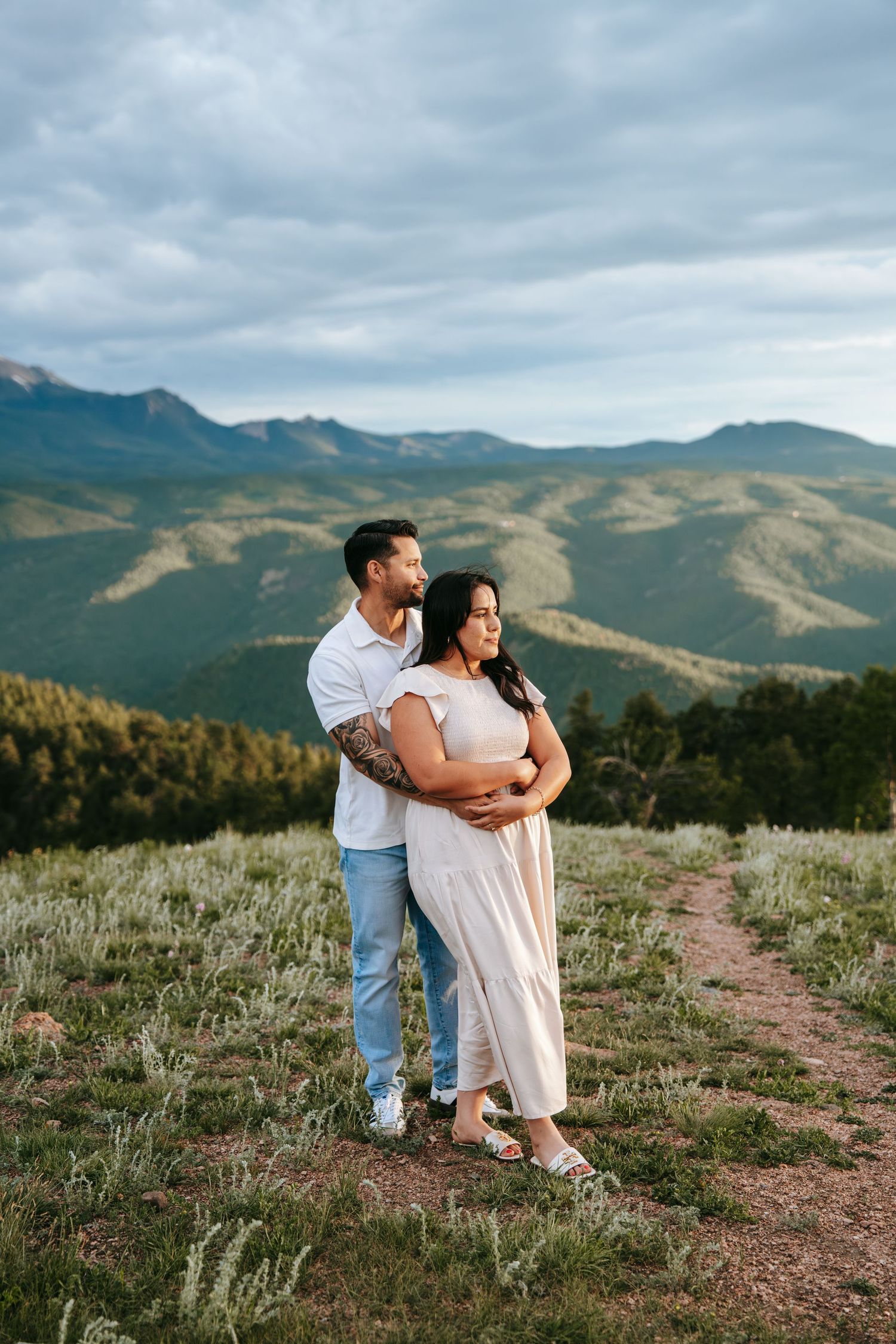 Couple embracing and gazing at scenic green mountain landscape on a cloudy summer day.